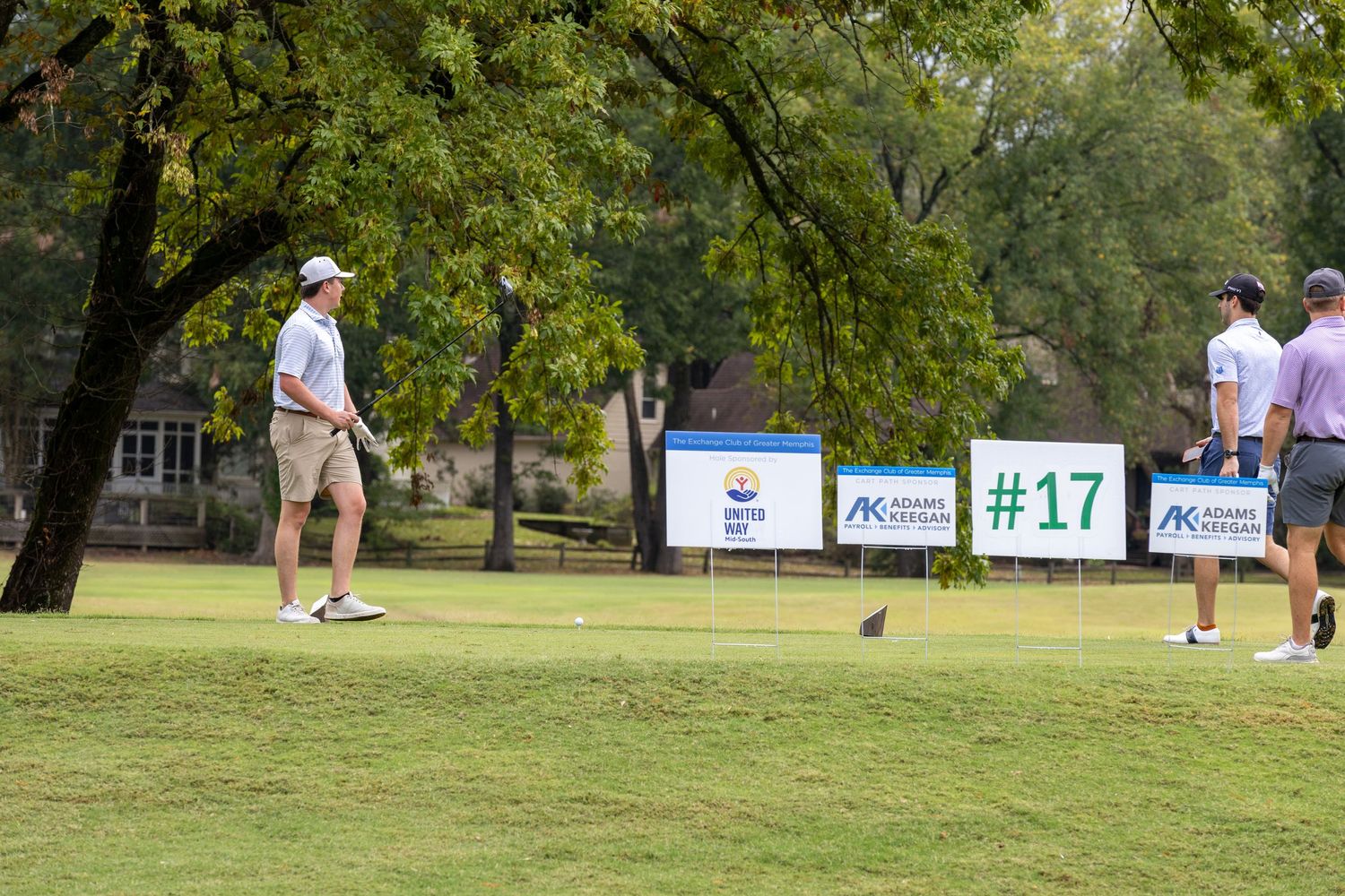 Golf tournament setup with sponsor signs and players on a green course.