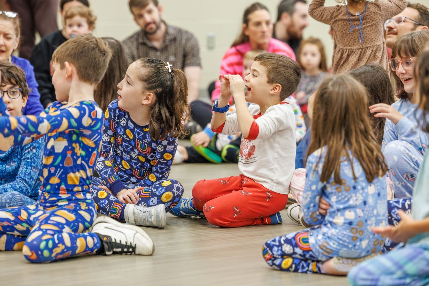 Children sitting on the floor in a classroom wearing colorful pajamas during a special school activity.