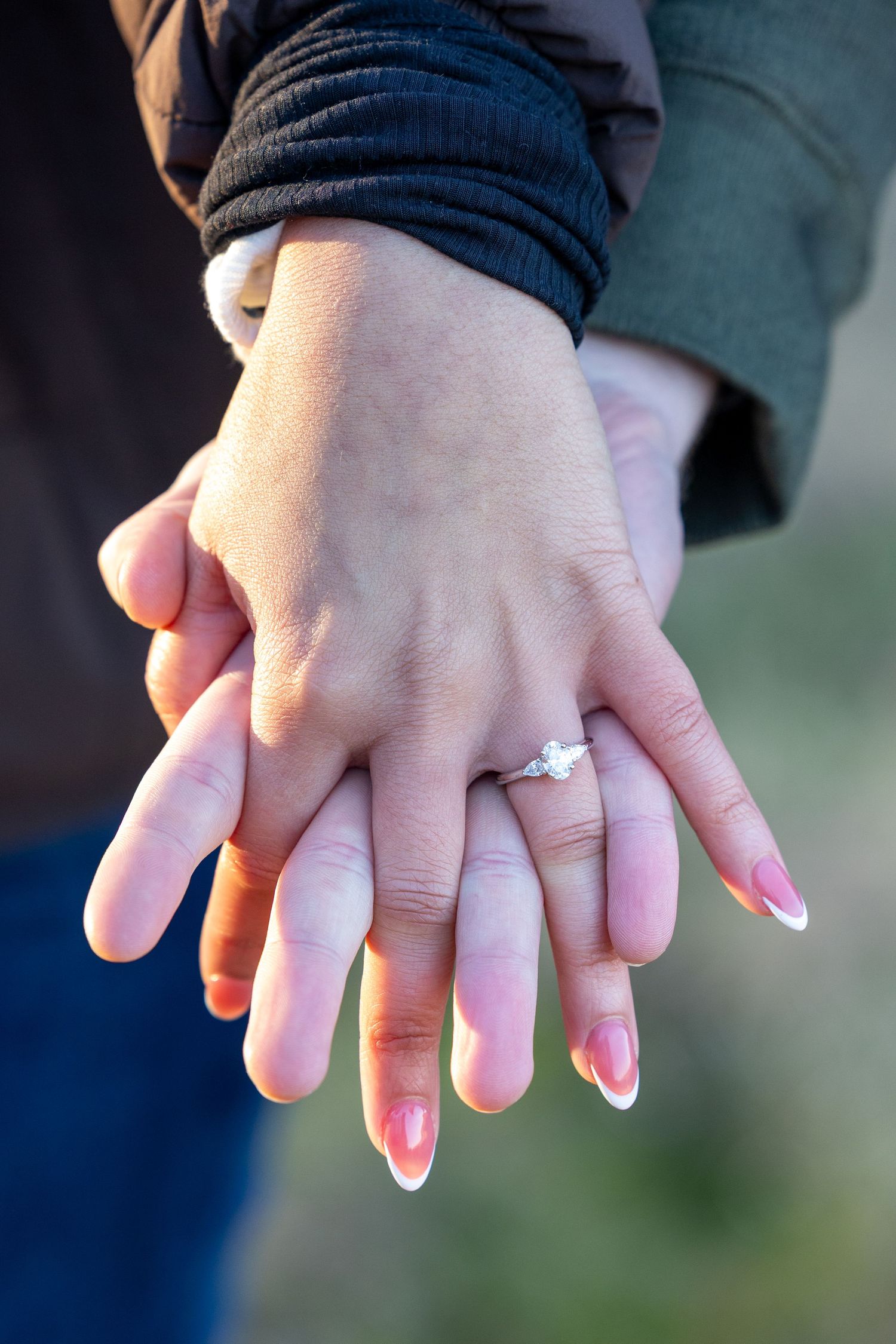 Close-up of two hands with engagement ring and pink manicure.