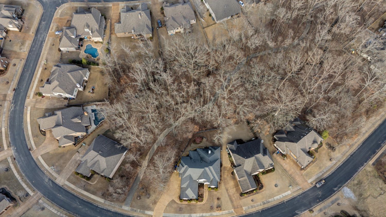 Aerial panoramic view of a curved suburban road winding through a residential neighborhood in winter.