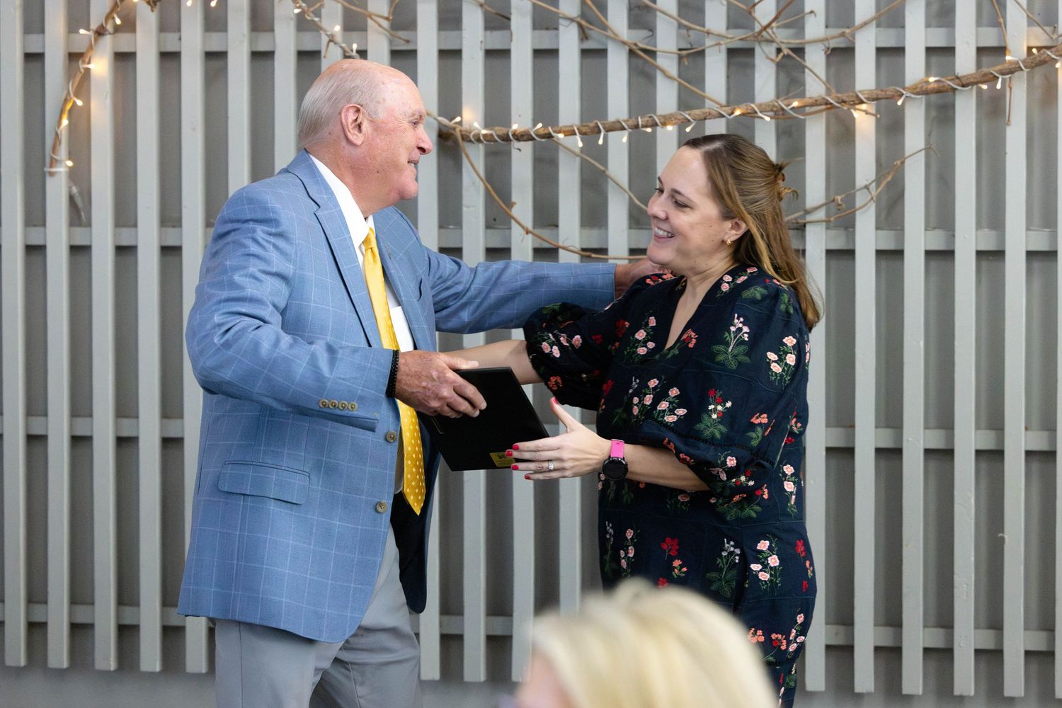 Two people in business attire engage in an animated conversation in front of a striped wall background.