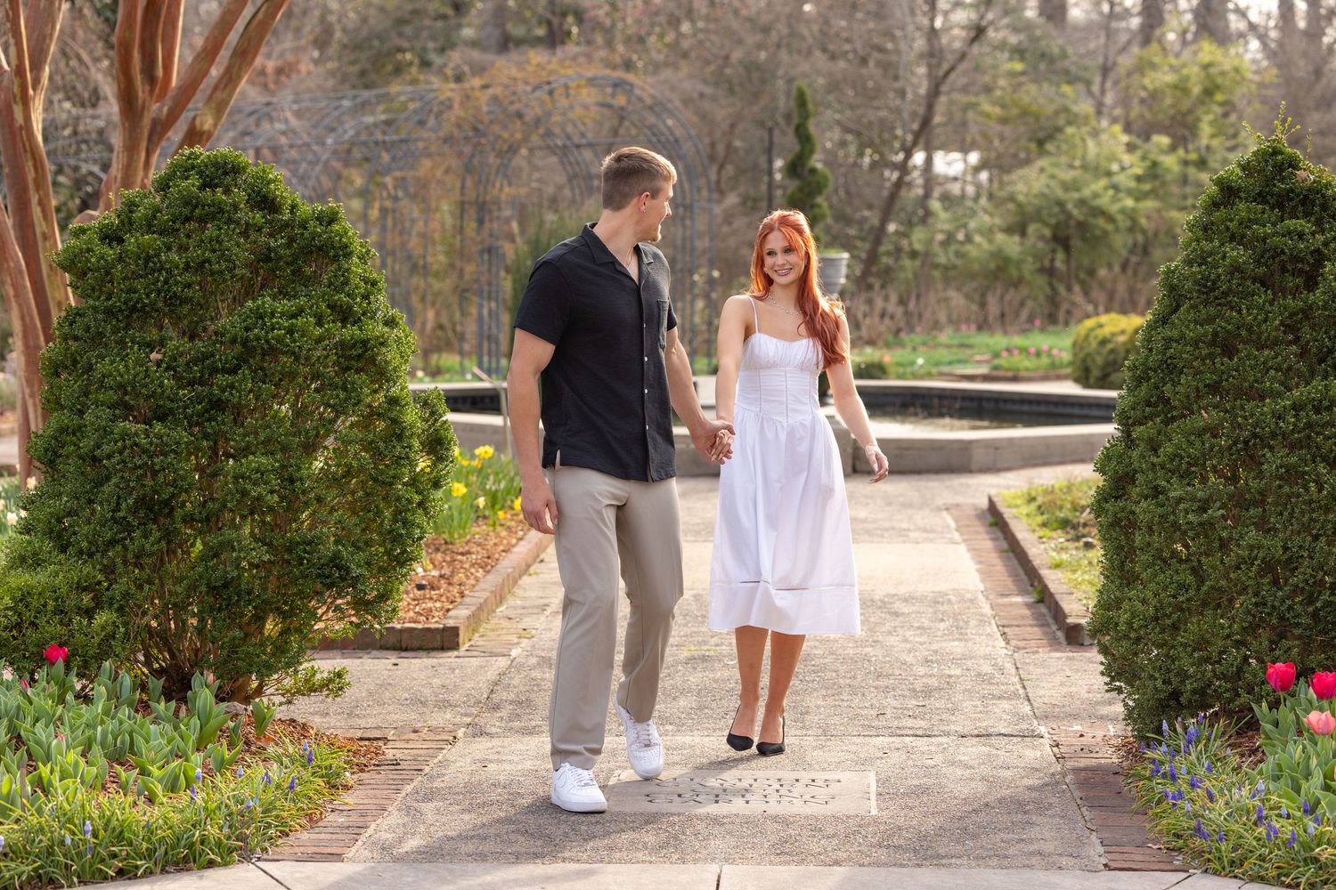 Couple walking together through a garden pathway surrounded by greenery and blooming flowers.