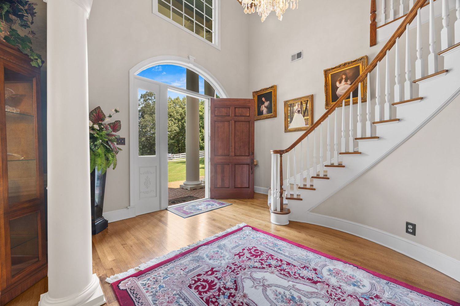 Elegant white staircase with wooden handrails and hardwood floors in a bright foyer with chandelier lighting.