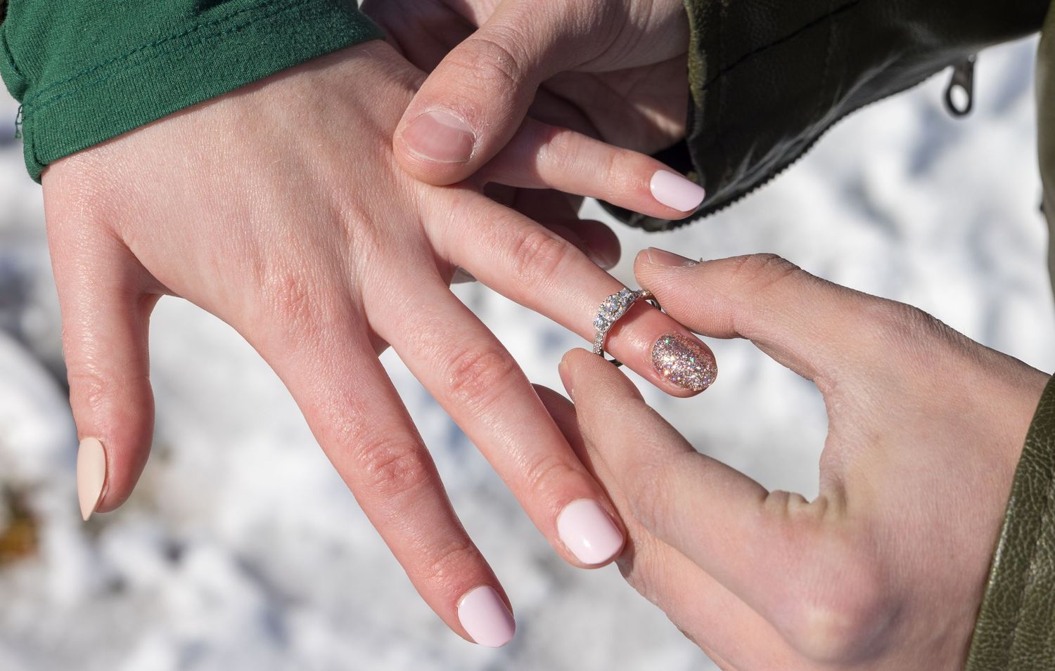 Close-up of hands placing an engagement ring on a finger with snow in the background.