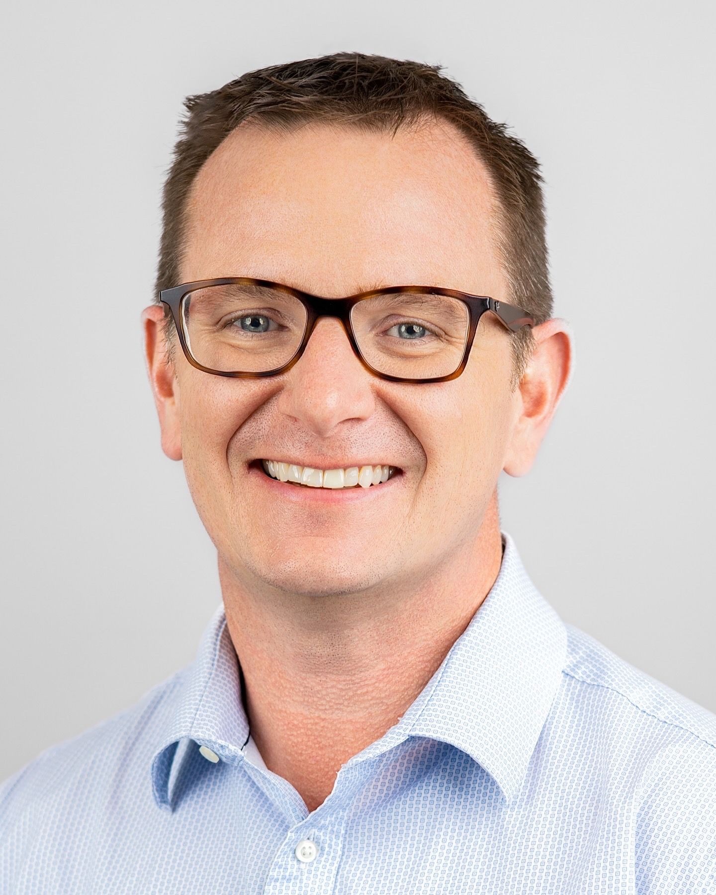 Professional headshots of person in light blue button-down shirt and glasses.