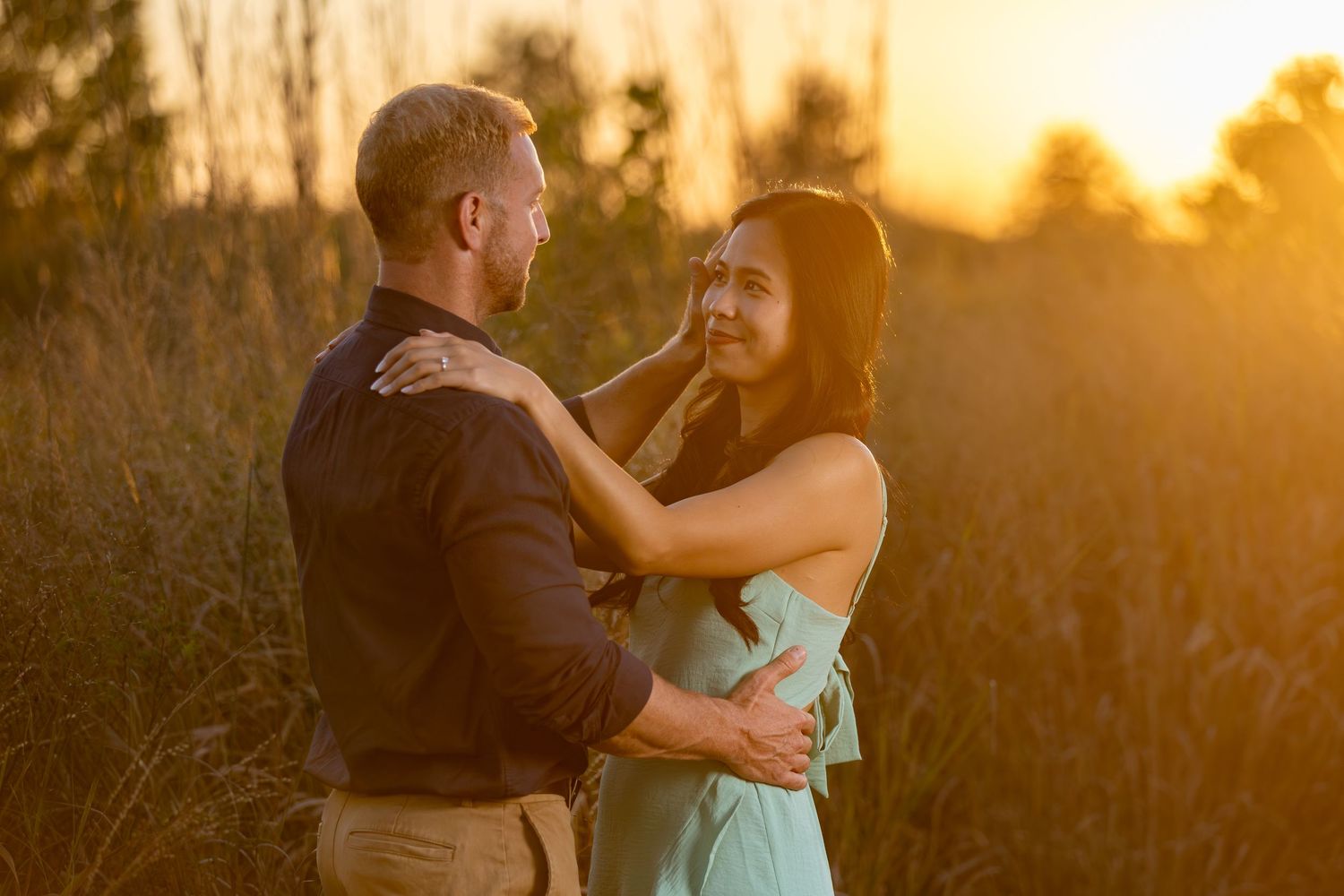 A couple shares a romantic moment in a field during golden sunset.