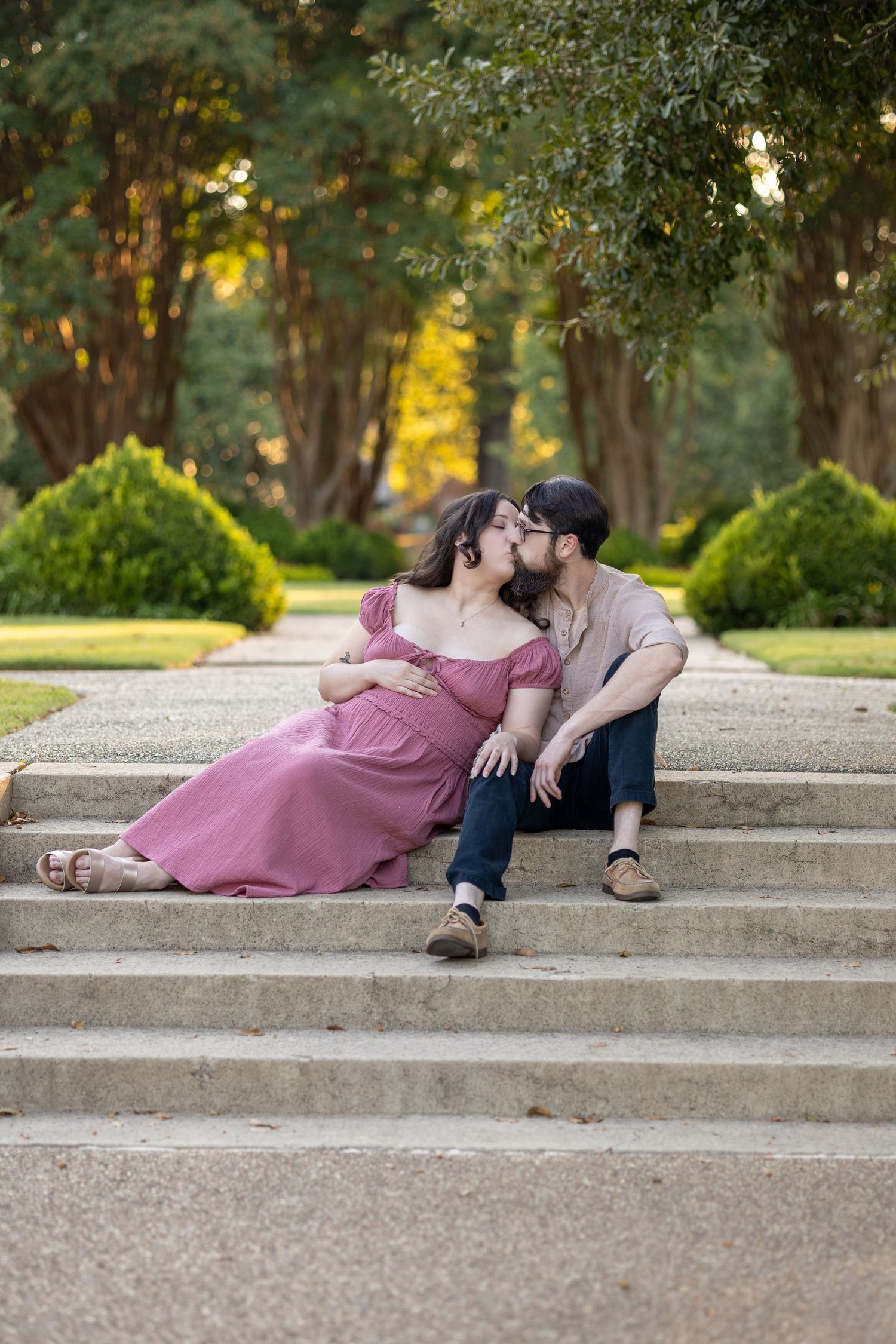 A romantic couple poses on concrete steps in a park setting during a photo session at sunset.