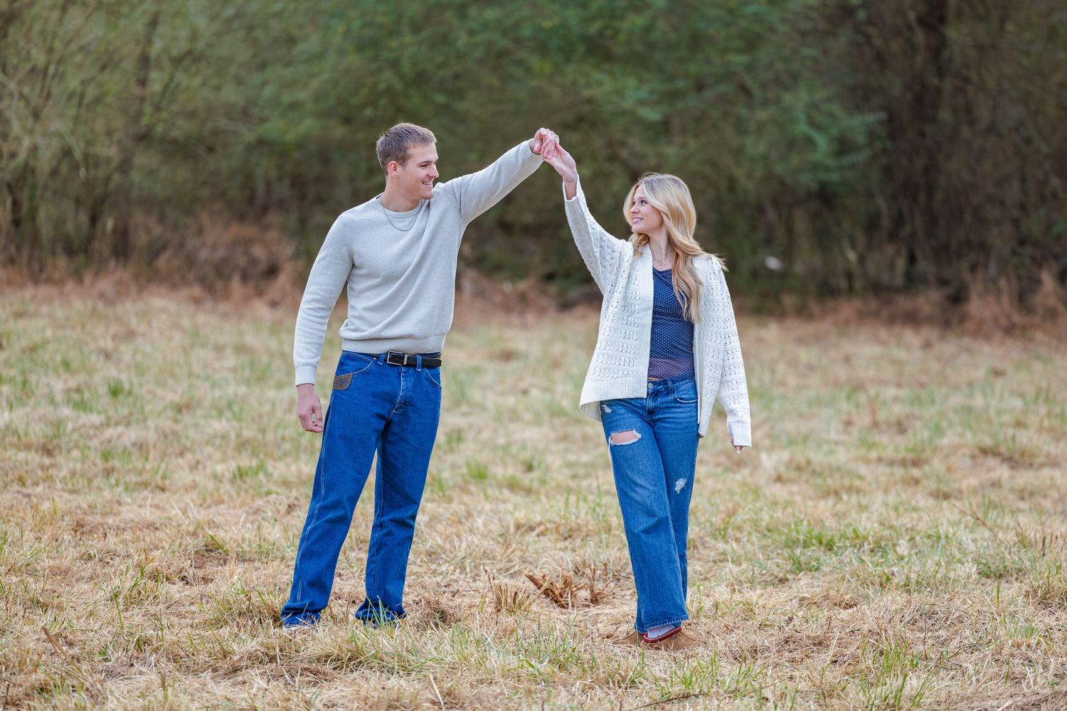 A couple walking hand in hand through a peaceful meadow wearing matching casual attire.