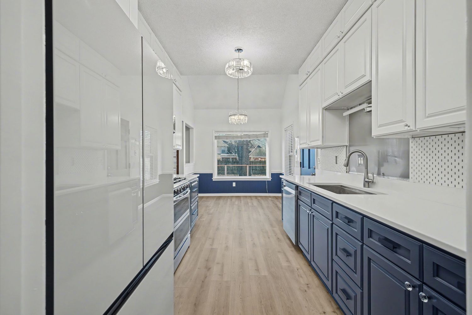 Modern galley kitchen with white upper cabinets, navy blue lower cabinets, light wood floors and white quartz countertops.