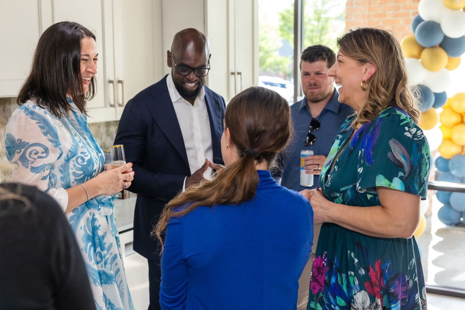Professionals networking at an indoor event with balloons, holding drinks and engaged in conversation.