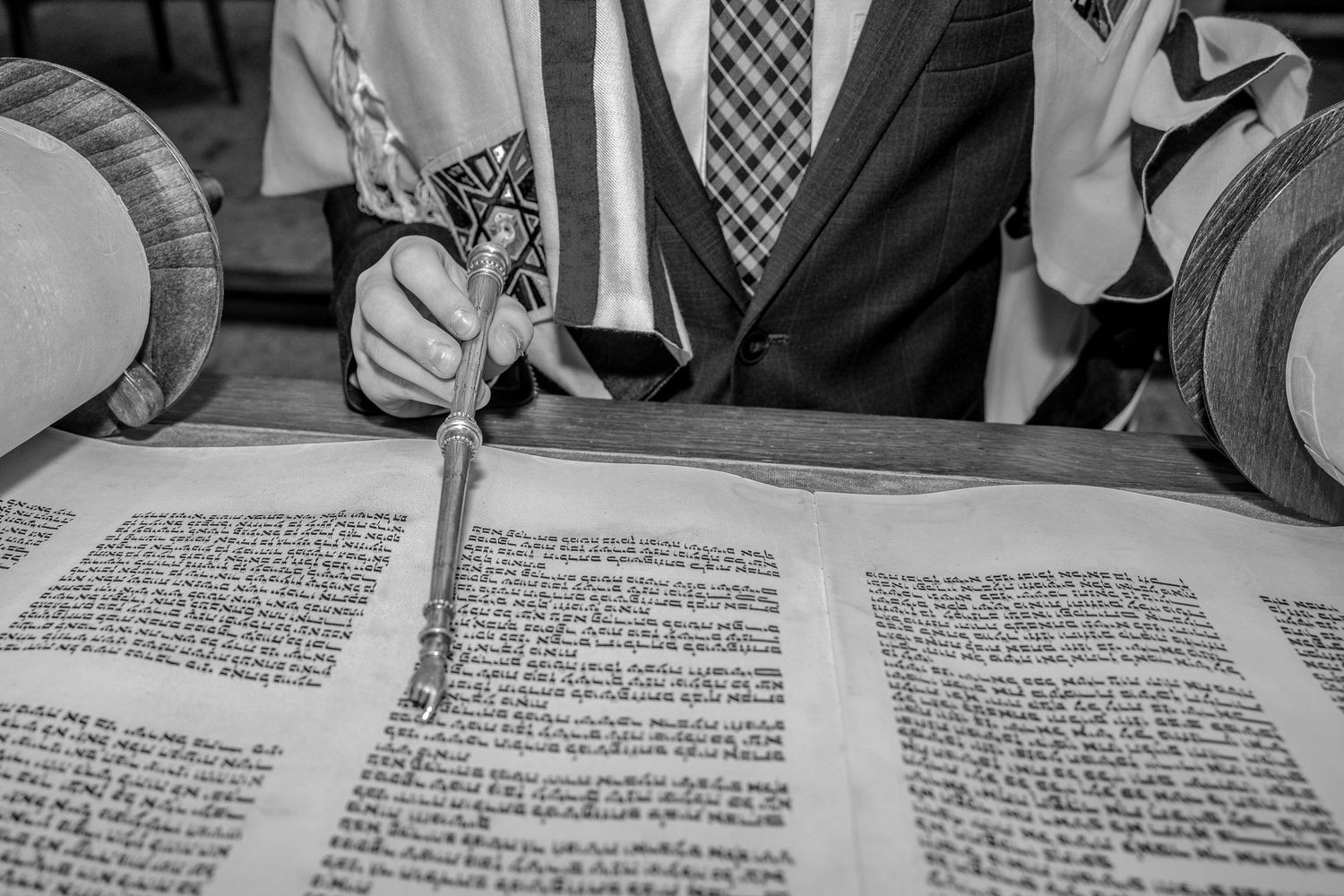 Man reading Torah scroll with a yad pointer during a Jewish religious ceremony, black and white photo.