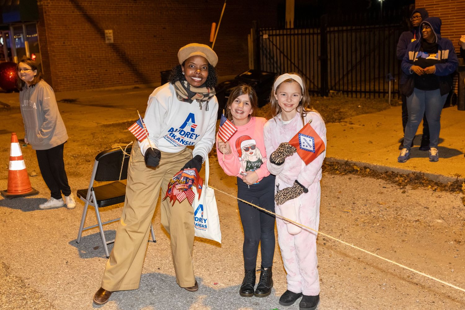 Three people pose together at a nighttime outdoor community event.