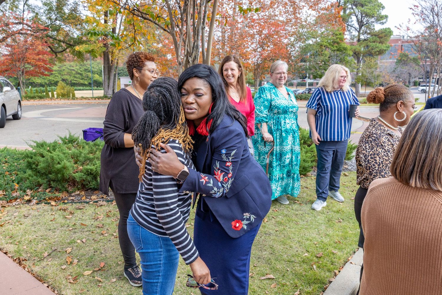 Attendees gather outdoors among fall trees during daytime community event.