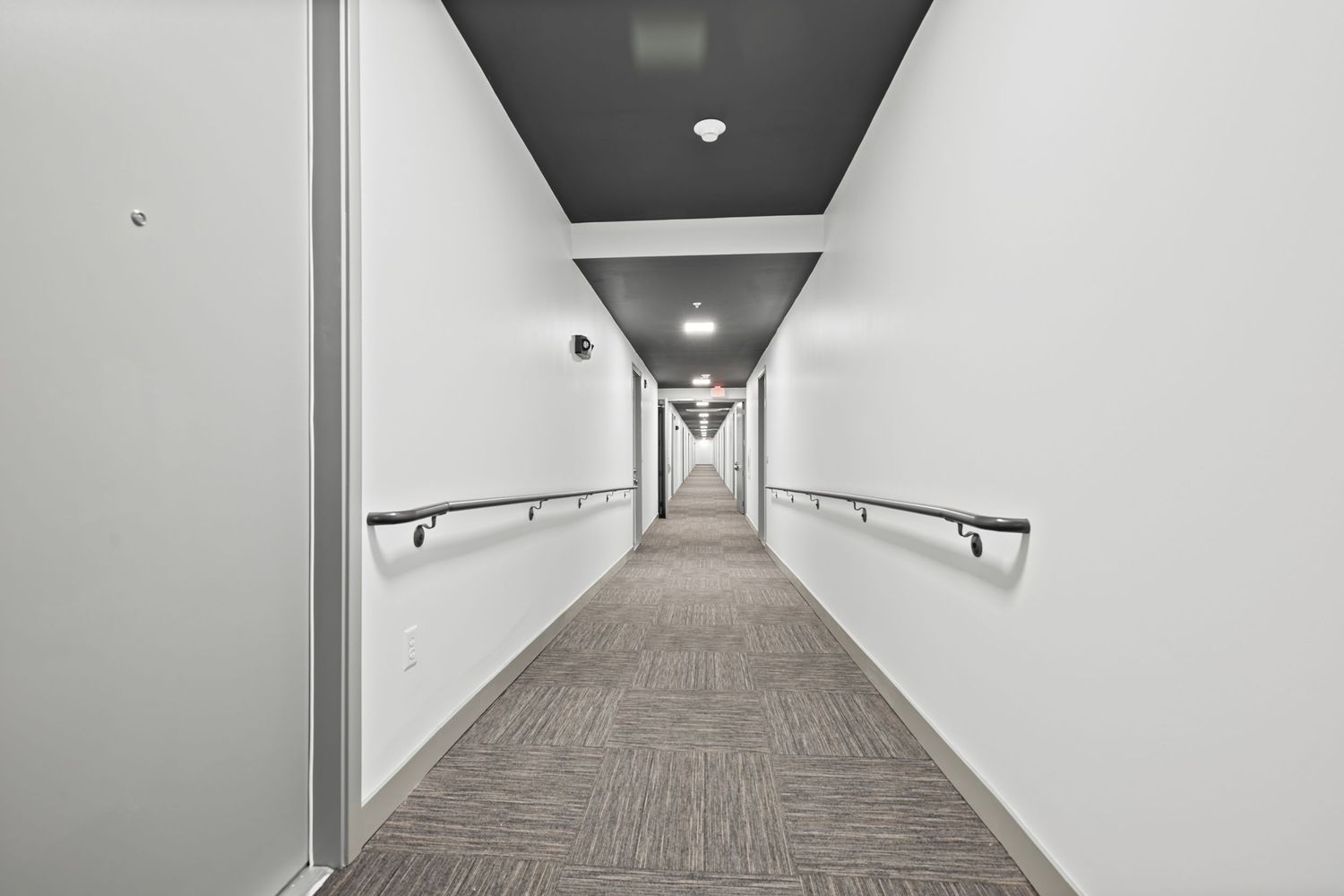 Commercial hallway with gray carpet, white walls, and modern lighting fixtures.