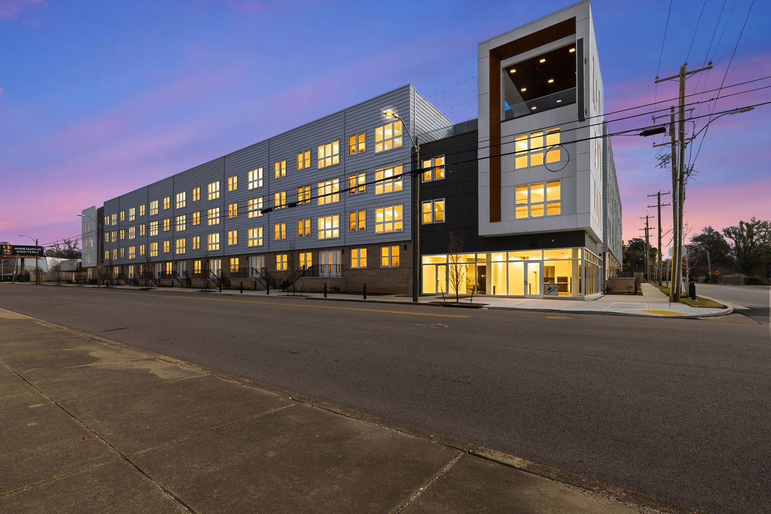 Modern apartment complex illuminated at dusk with glowing windows and parking area.
