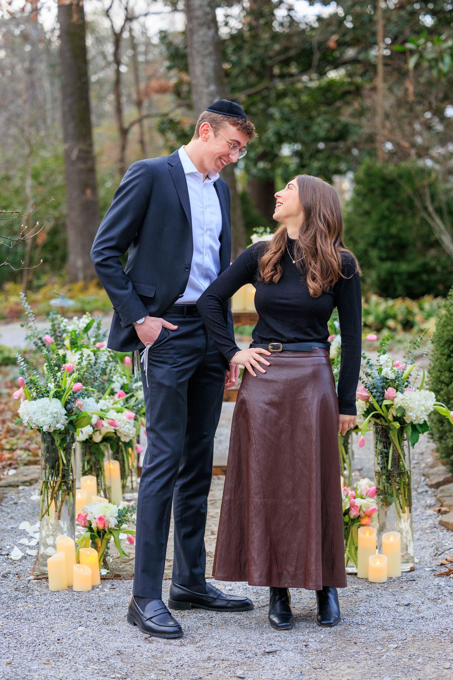 A romantic outdoor proposal scene with lanterns and floral decorations along a gravel path at dusk.