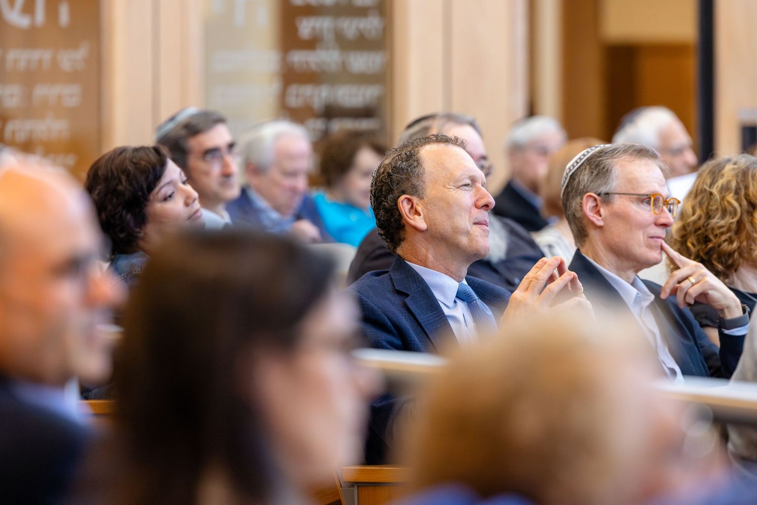 Audience members engaged in a formal lecture or conference event, seated in rows inside an elegant hall.