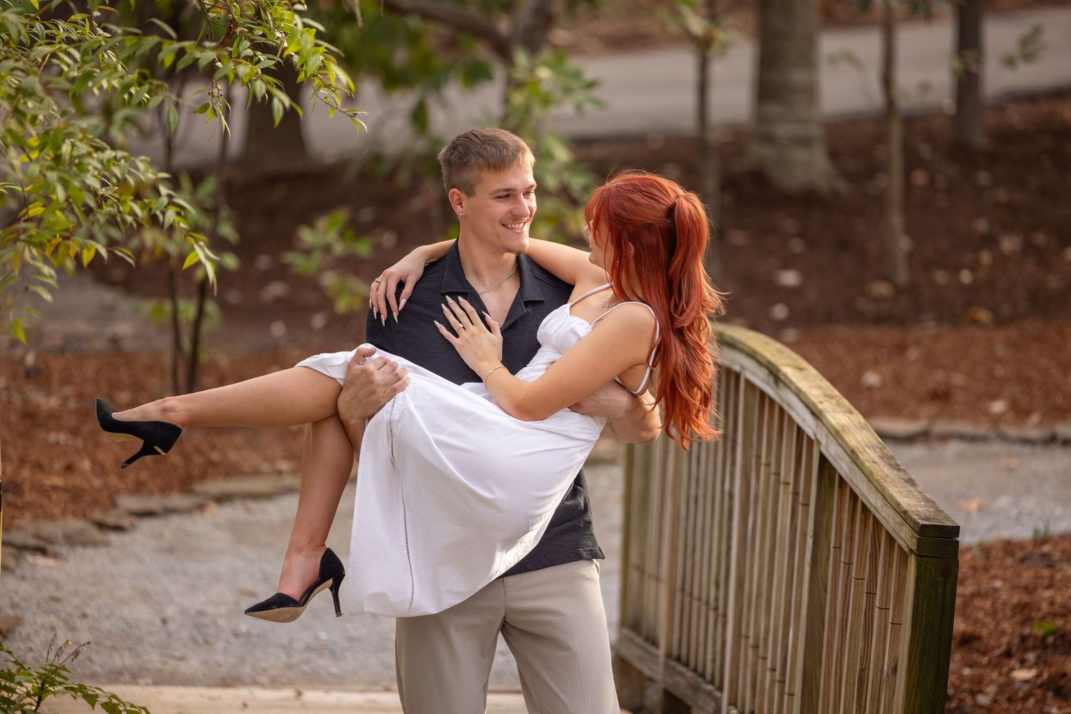 Couple dances together in a romantic outdoor setting with wooden fence and greenery in background.