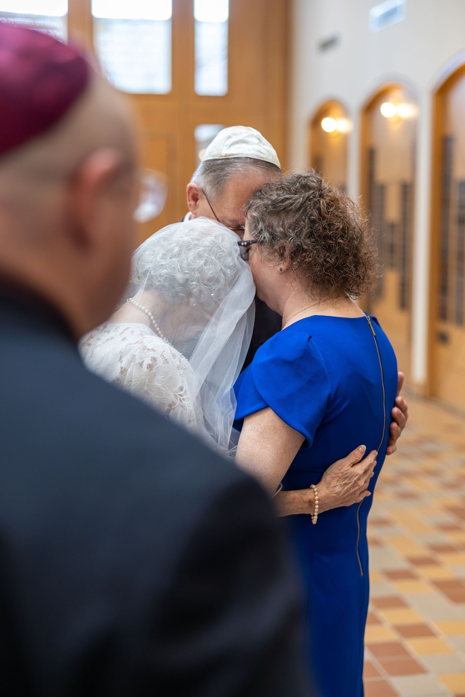 Two people embrace in an emotional moment during a ceremony in a church with tiled floors and arched windows.