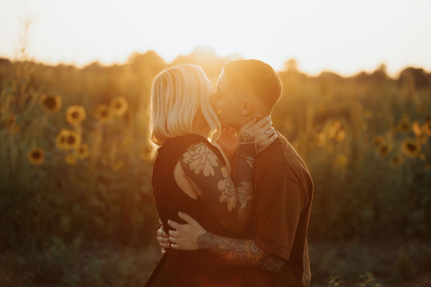 Silhouetted figures share a romantic moment among sunflowers during sunset.