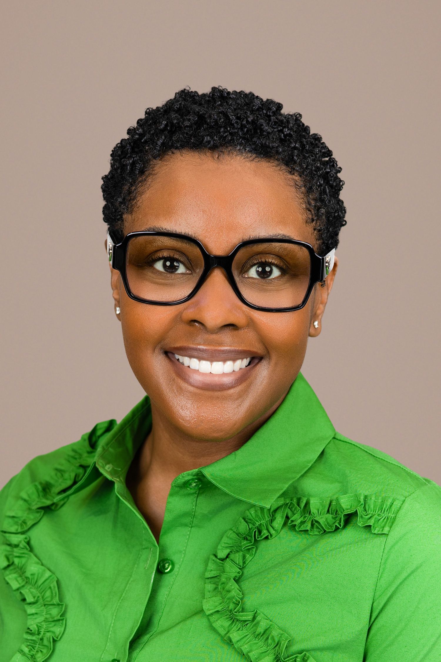 Professional headshot of someone wearing glasses and a bright green ruffled collar blouse against neutral background.