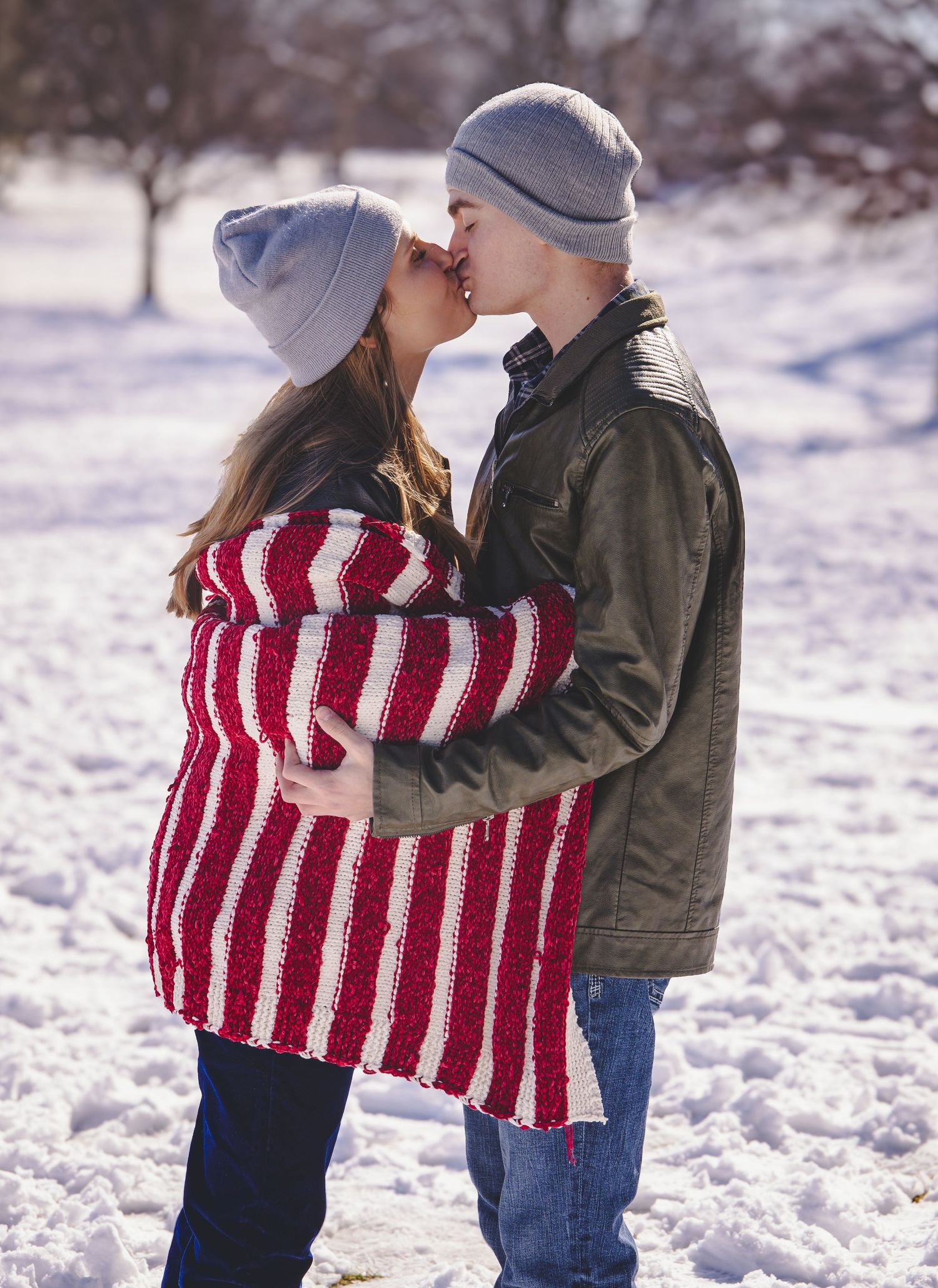 A winter engagement moment with a couple kissing in the snow wearing cozy outfits.