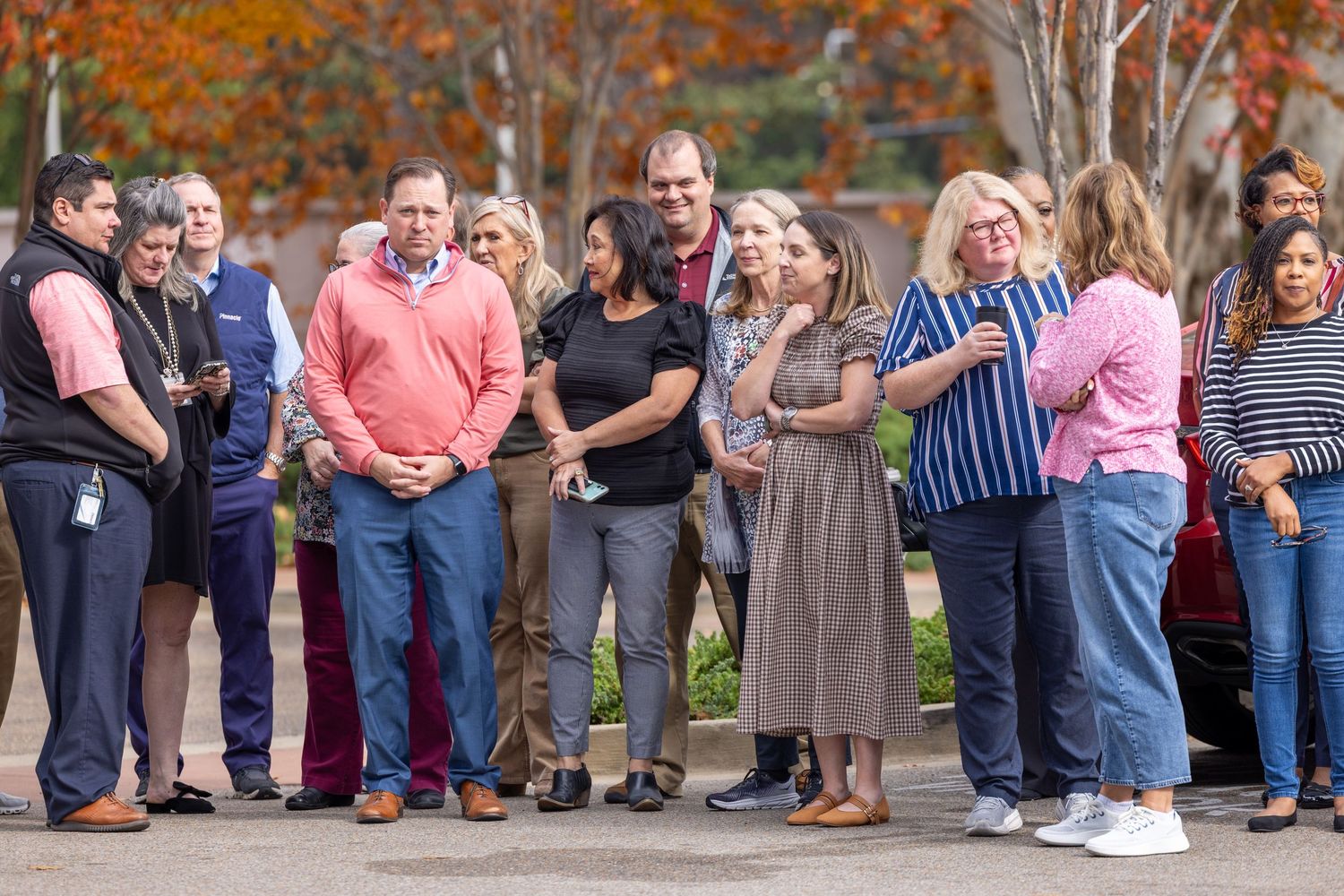 Large group stands together during outdoor community event in fall.