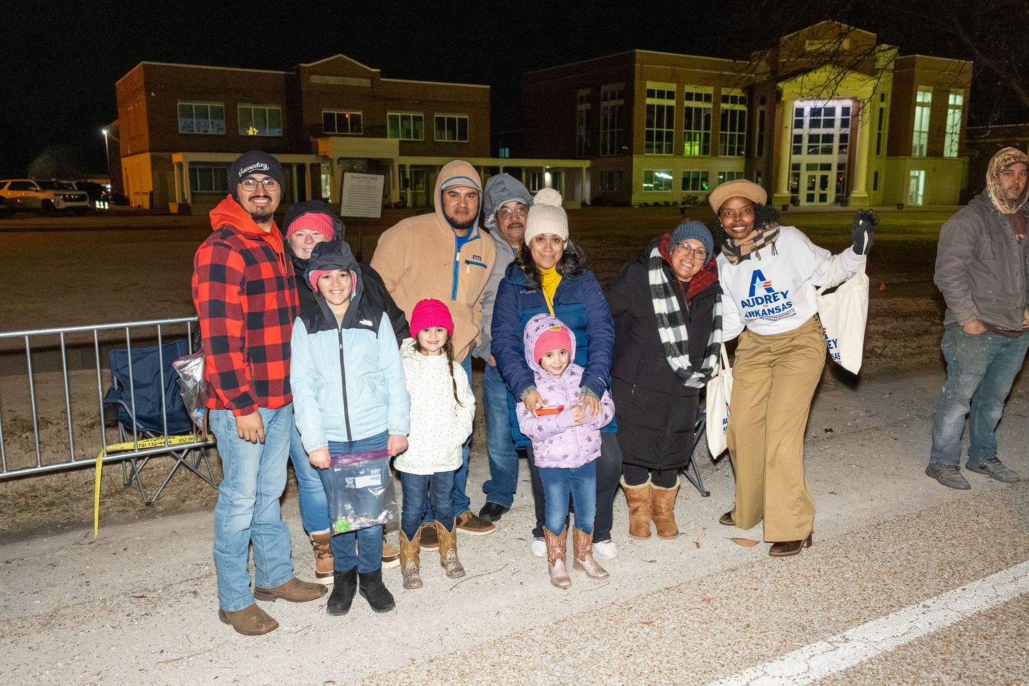Large group gathers outside at night for a community event in front of a building.