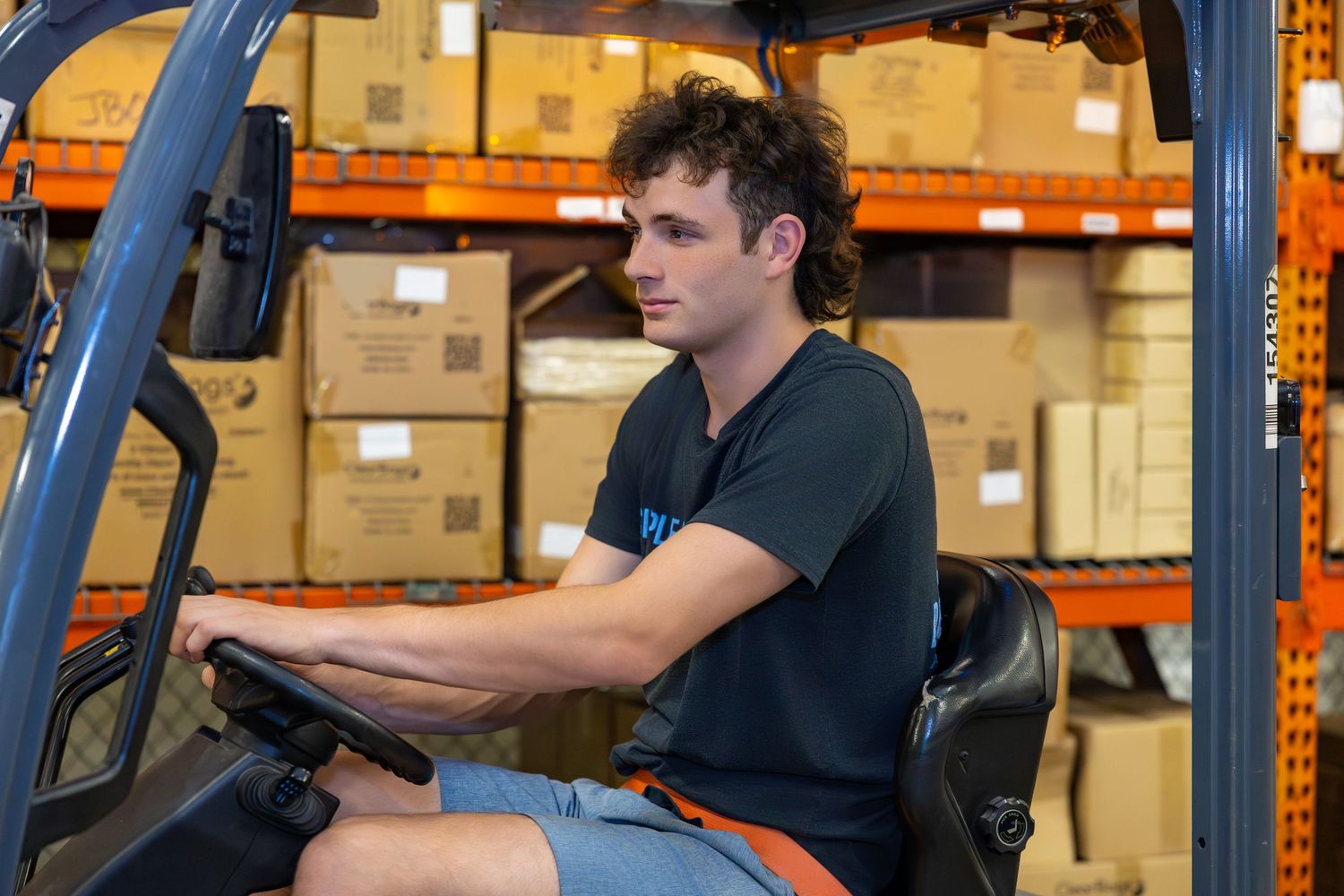 Forklift operator operating vehicle in warehouse storage facility.