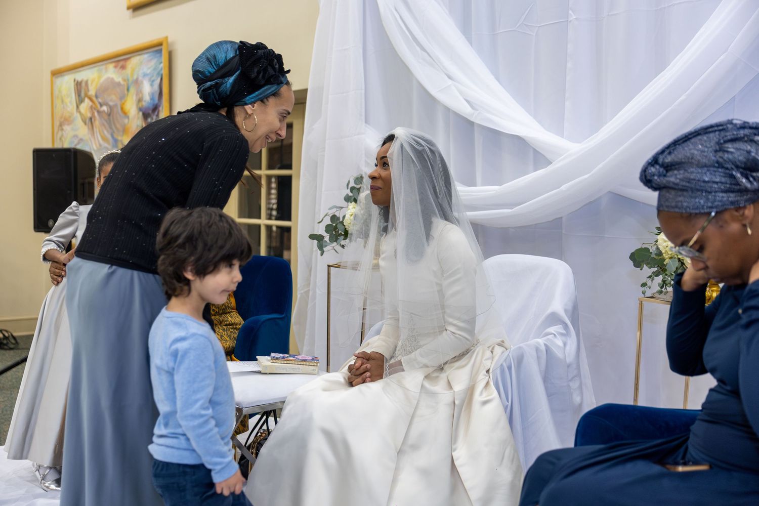 Wedding ceremony scene with white draping and guests gathered in an indoor venue.
