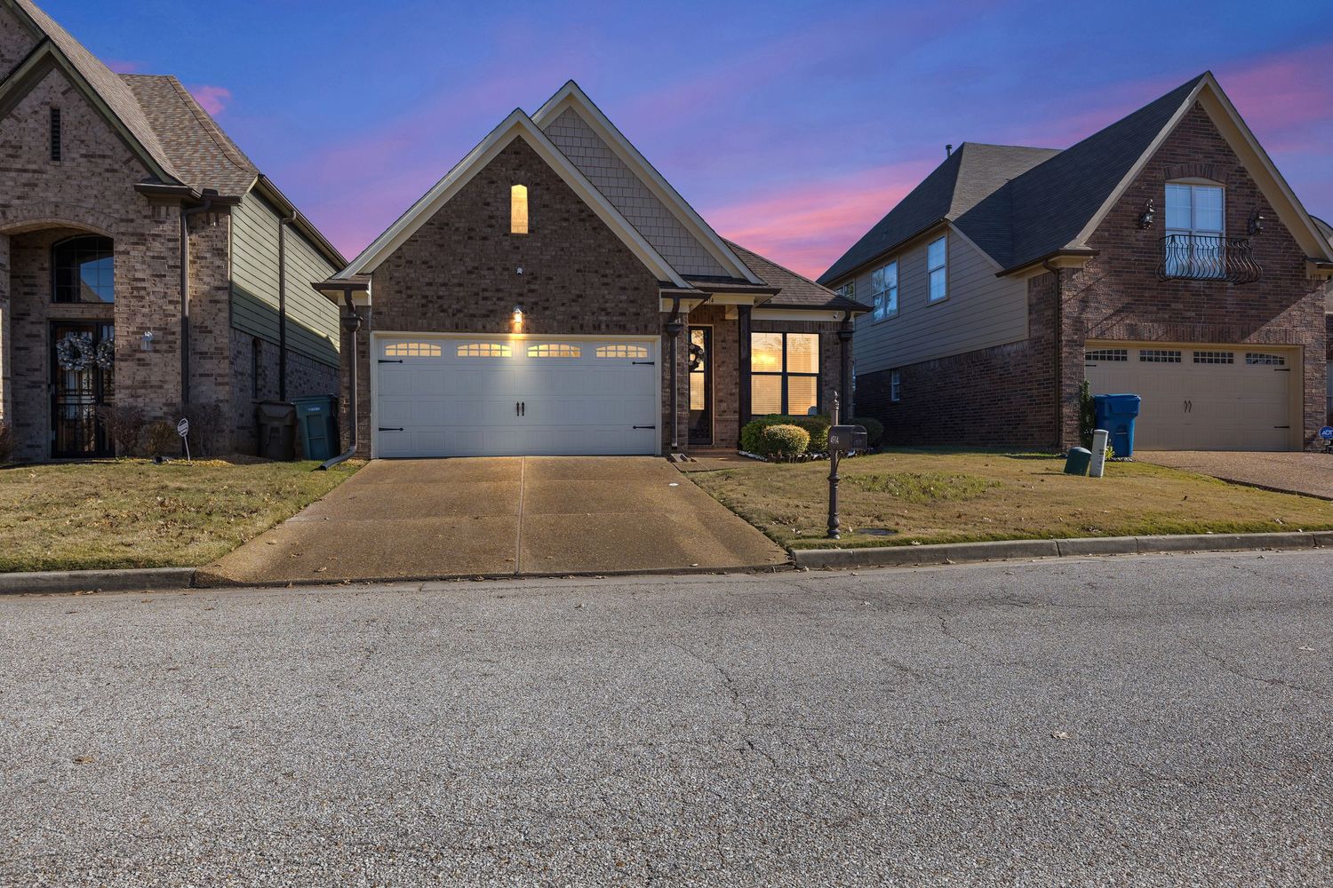 Suburban neighborhood houses at dusk with dramatic purple sky and street lights.