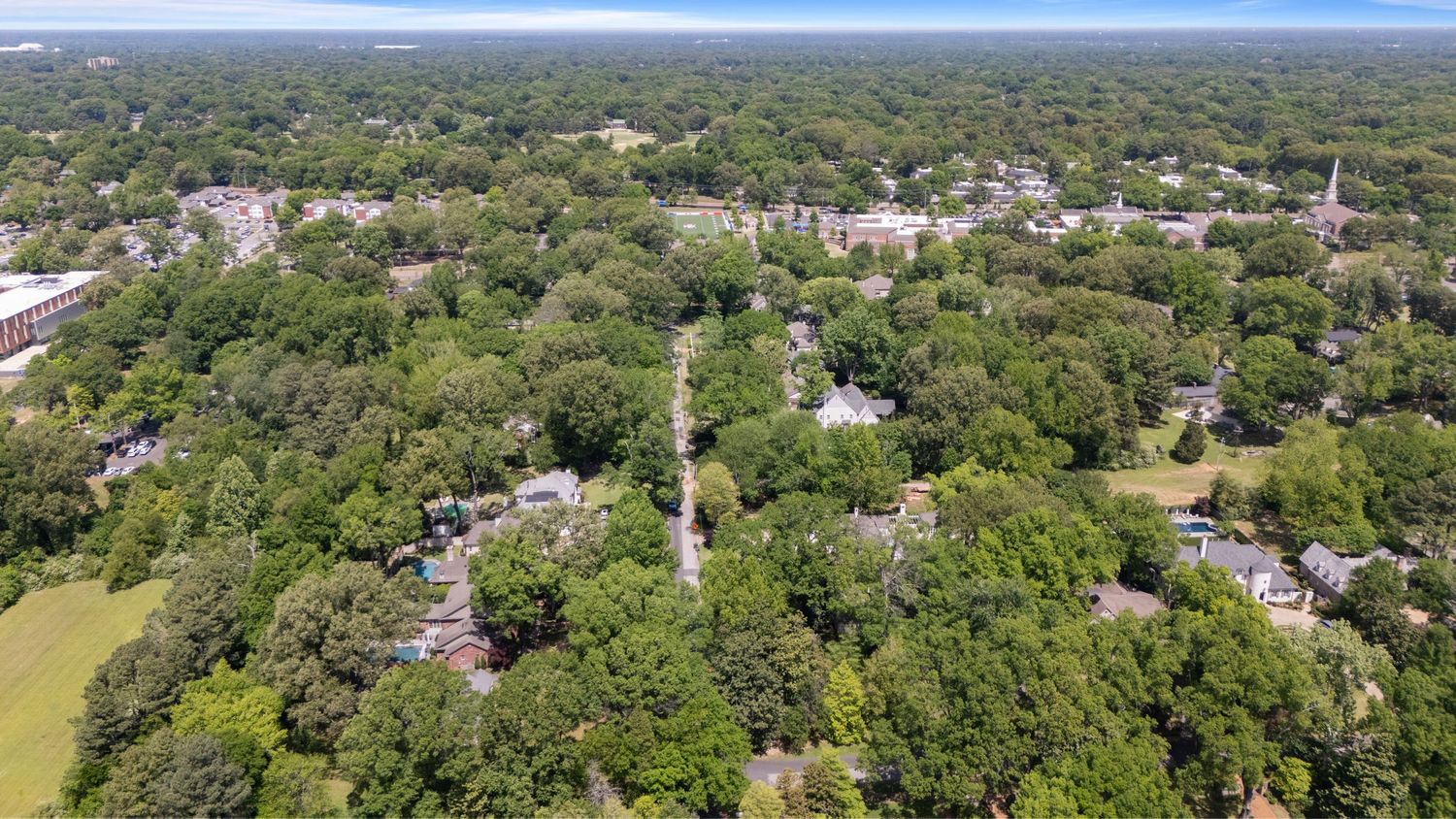 Aerial view of a lush green suburban neighborhood with tree-lined streets and residential homes surrounded by dense foliage.