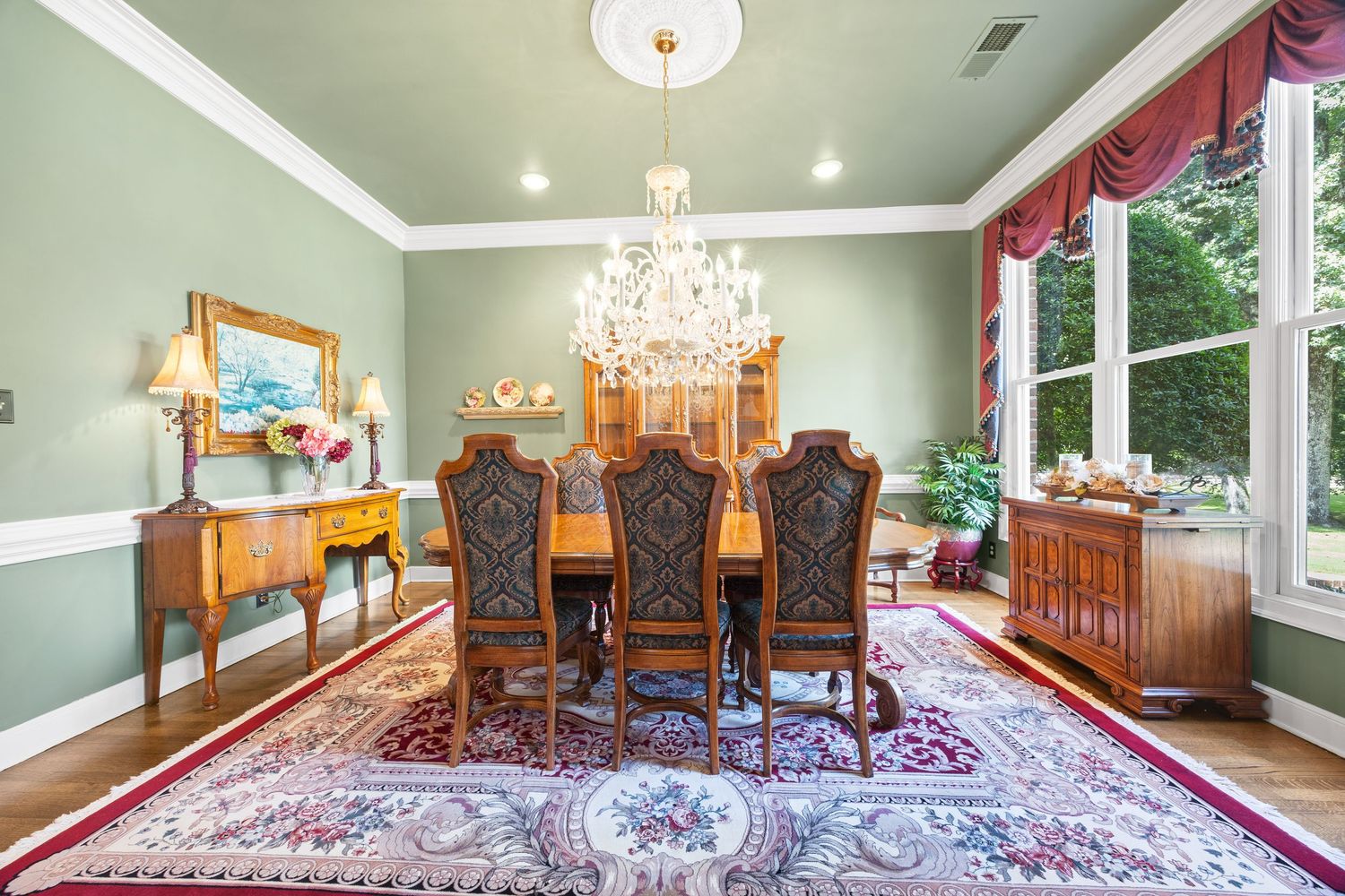 Elegant dining room with crystal chandelier, red curtains, and green walls.