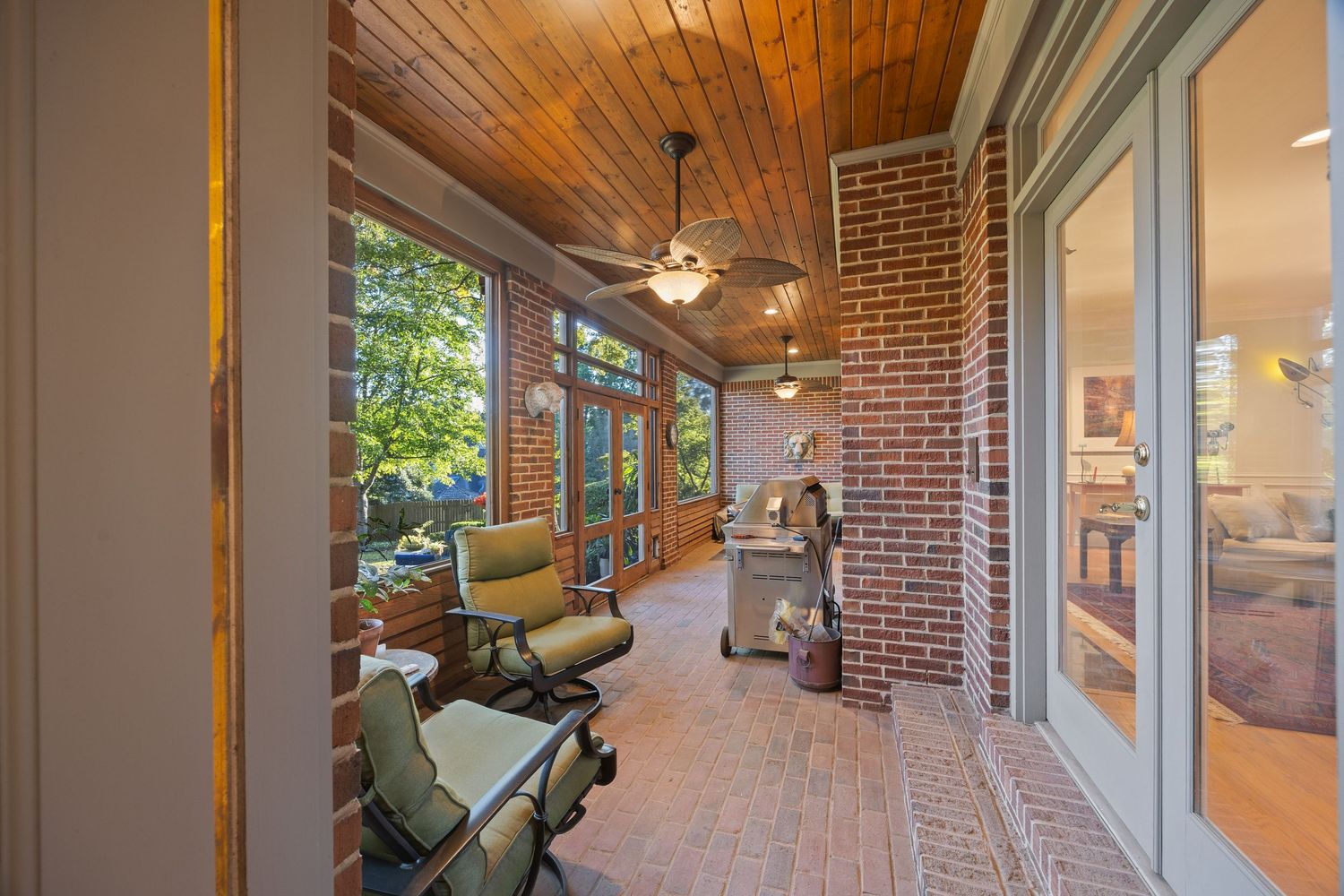 A panoramic view of a rustic covered porch with exposed wooden beams, brick columns, and comfortable outdoor furniture.