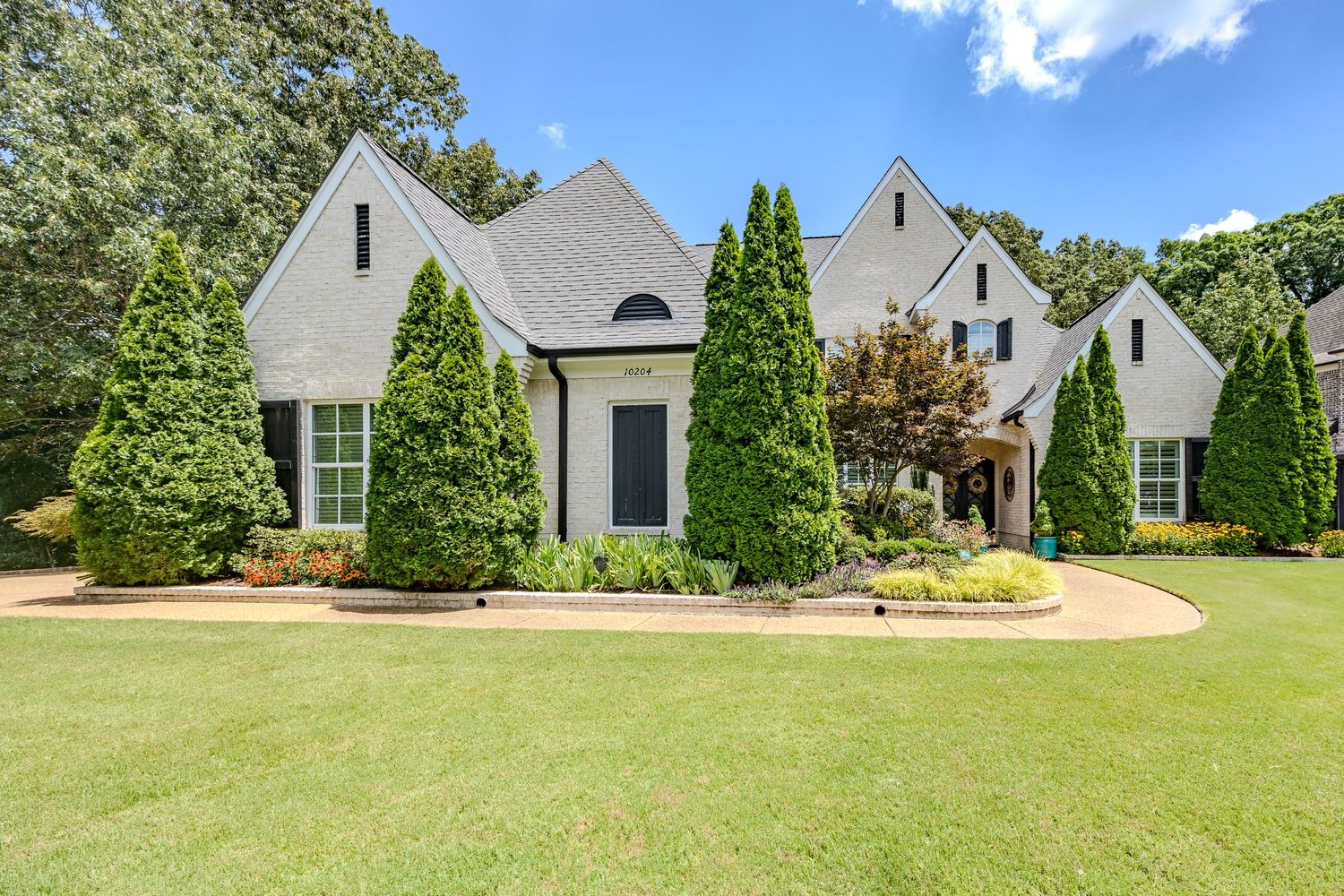 White farmhouse style home with gabled roof sits on expansive green lawn with mature trees and landscaping.