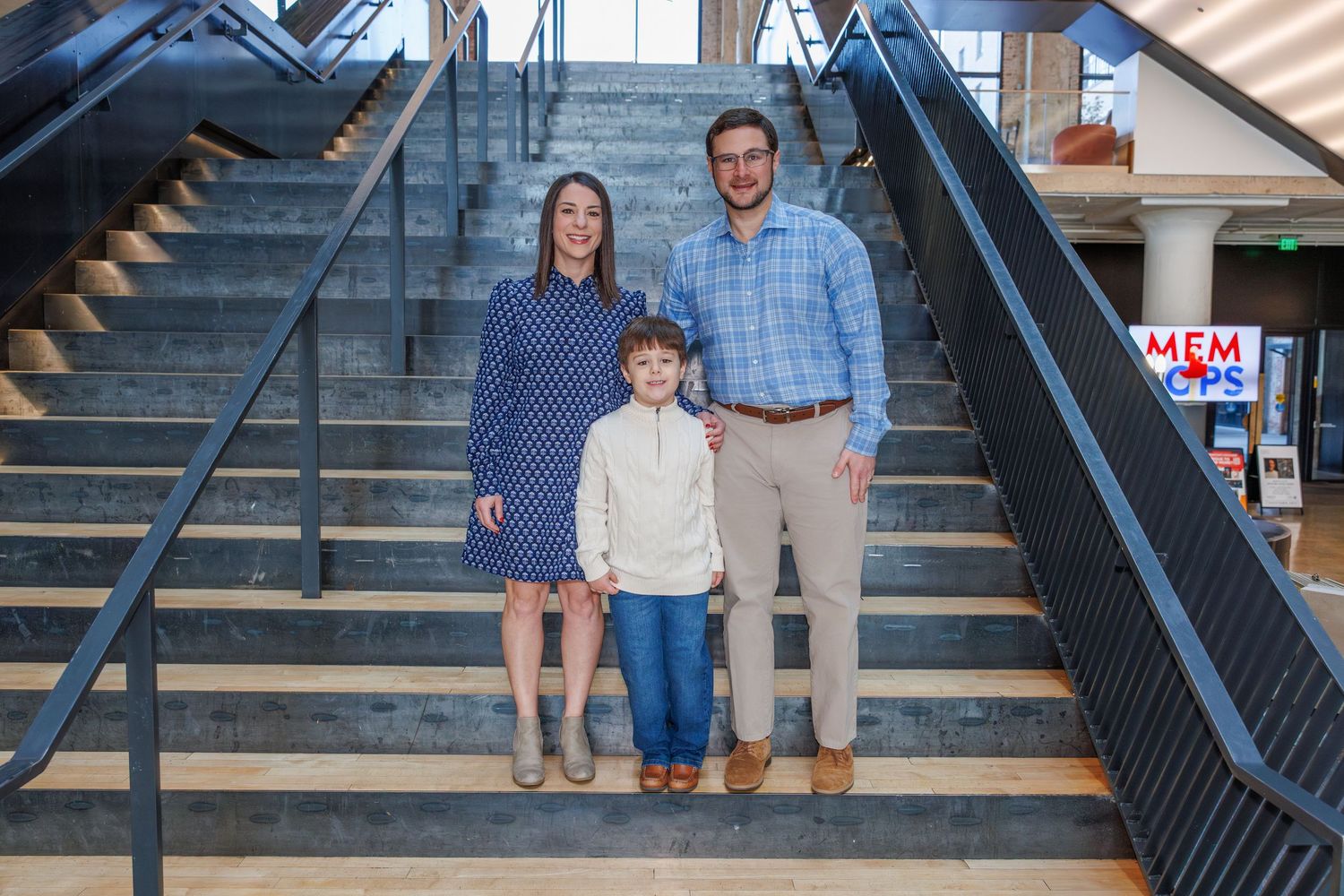 Group posing on industrial metal stairs against exposed brick wall.