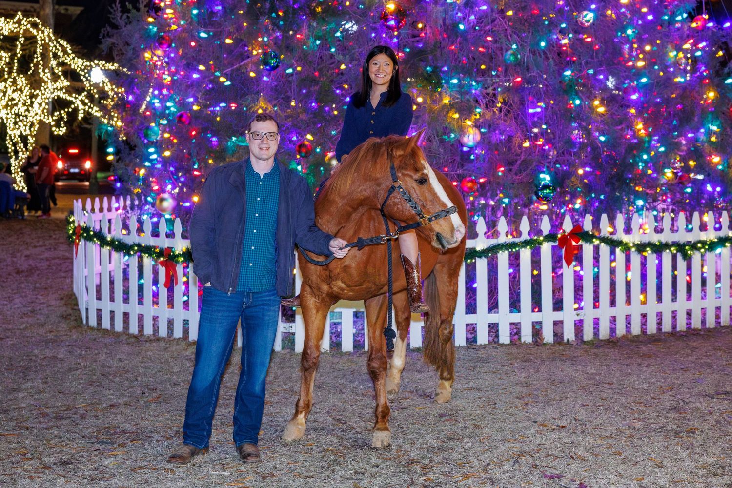 Colorful Christmas lights illuminate a festive outdoor display with a white picket fence.