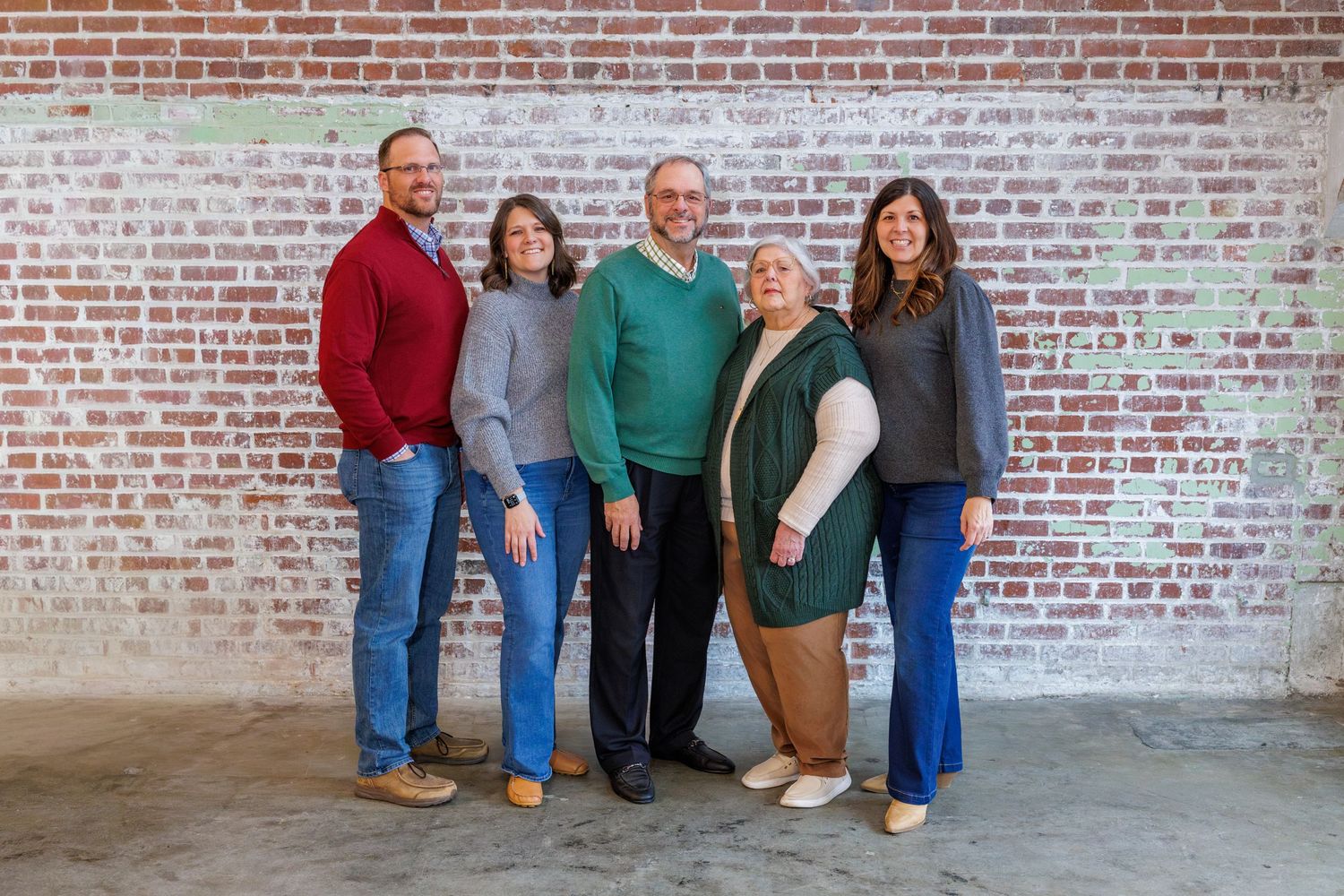 A group of people posing together against a rustic brick wall backdrop.