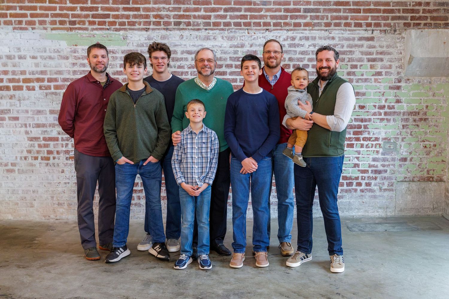 An extended family gathering poses together in casual attire against a textured brick wall background.