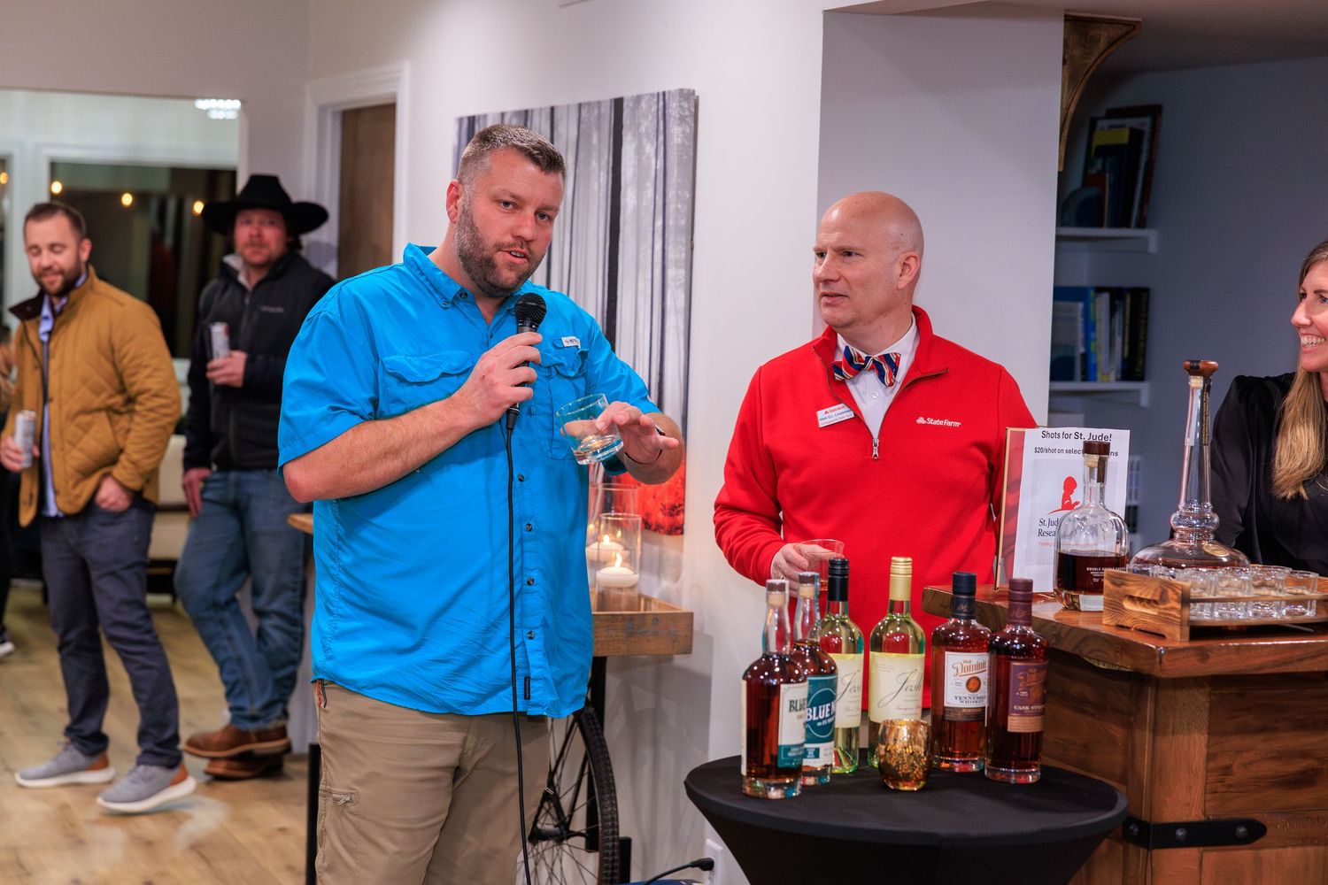Two people present spirits and beverages at a tasting event with bottles displayed on a wooden table.