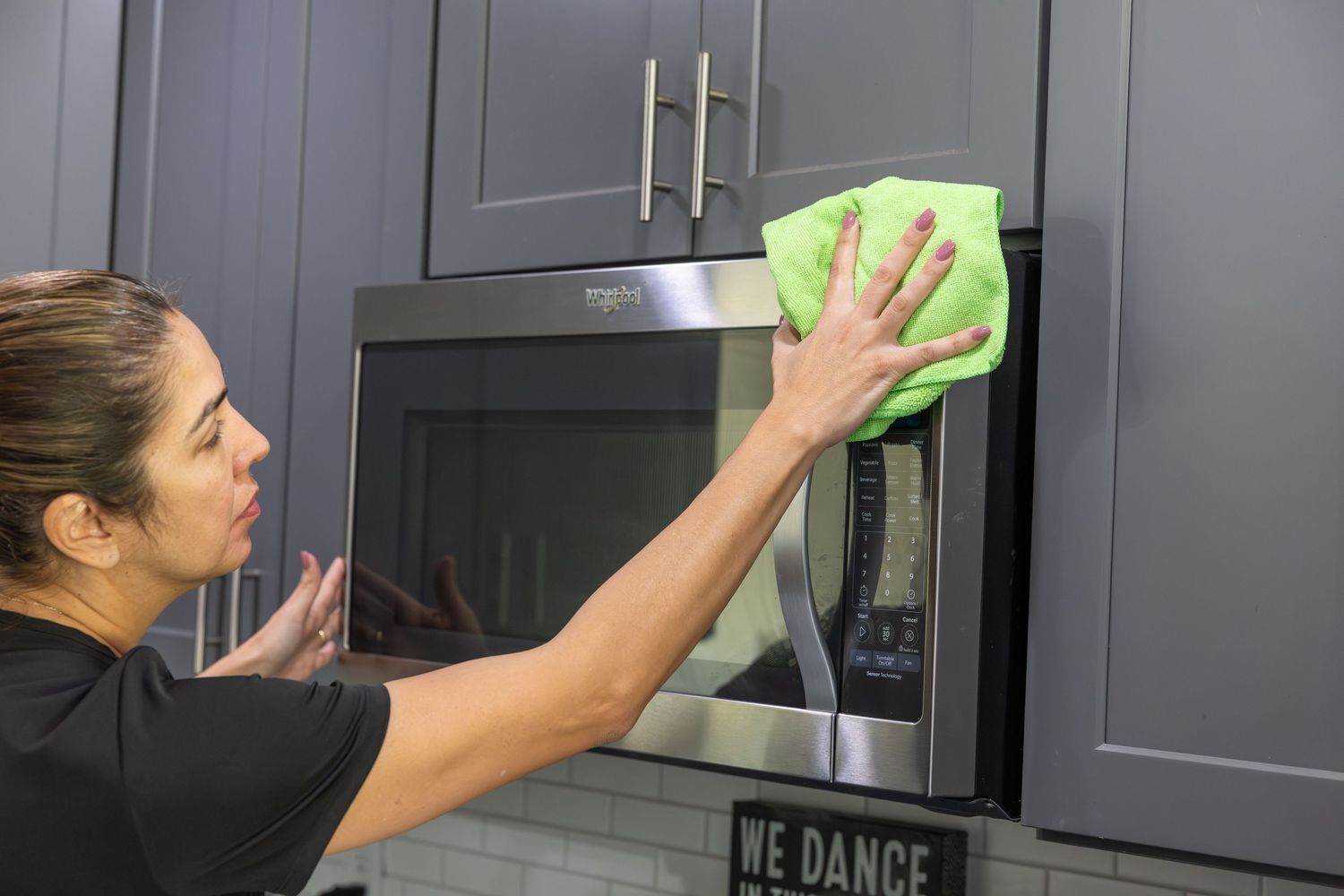 Professional cleaner wiping dark gray kitchen cabinets with green cloth.