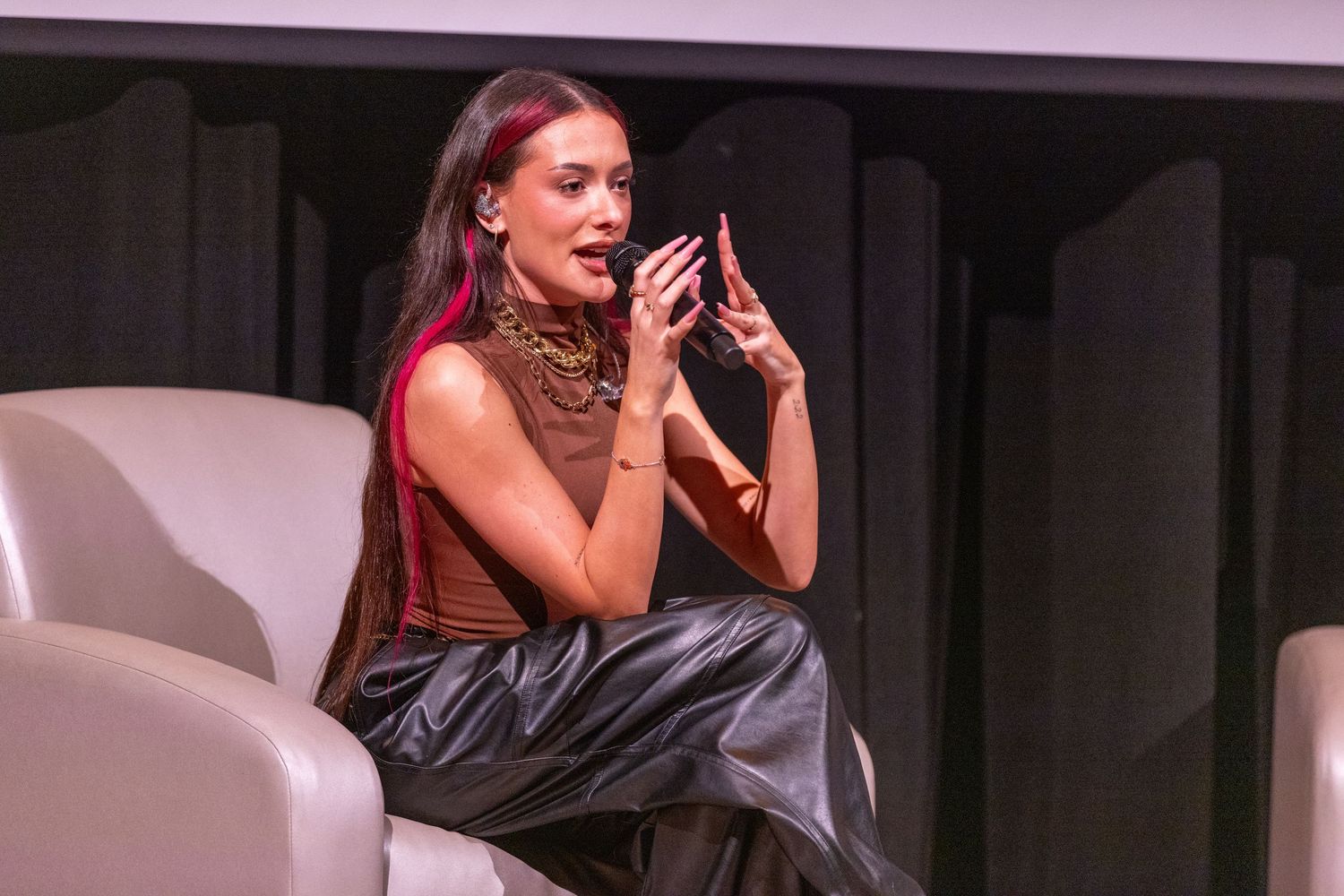 Singer in dark outfit performs emotively on illuminated stage.