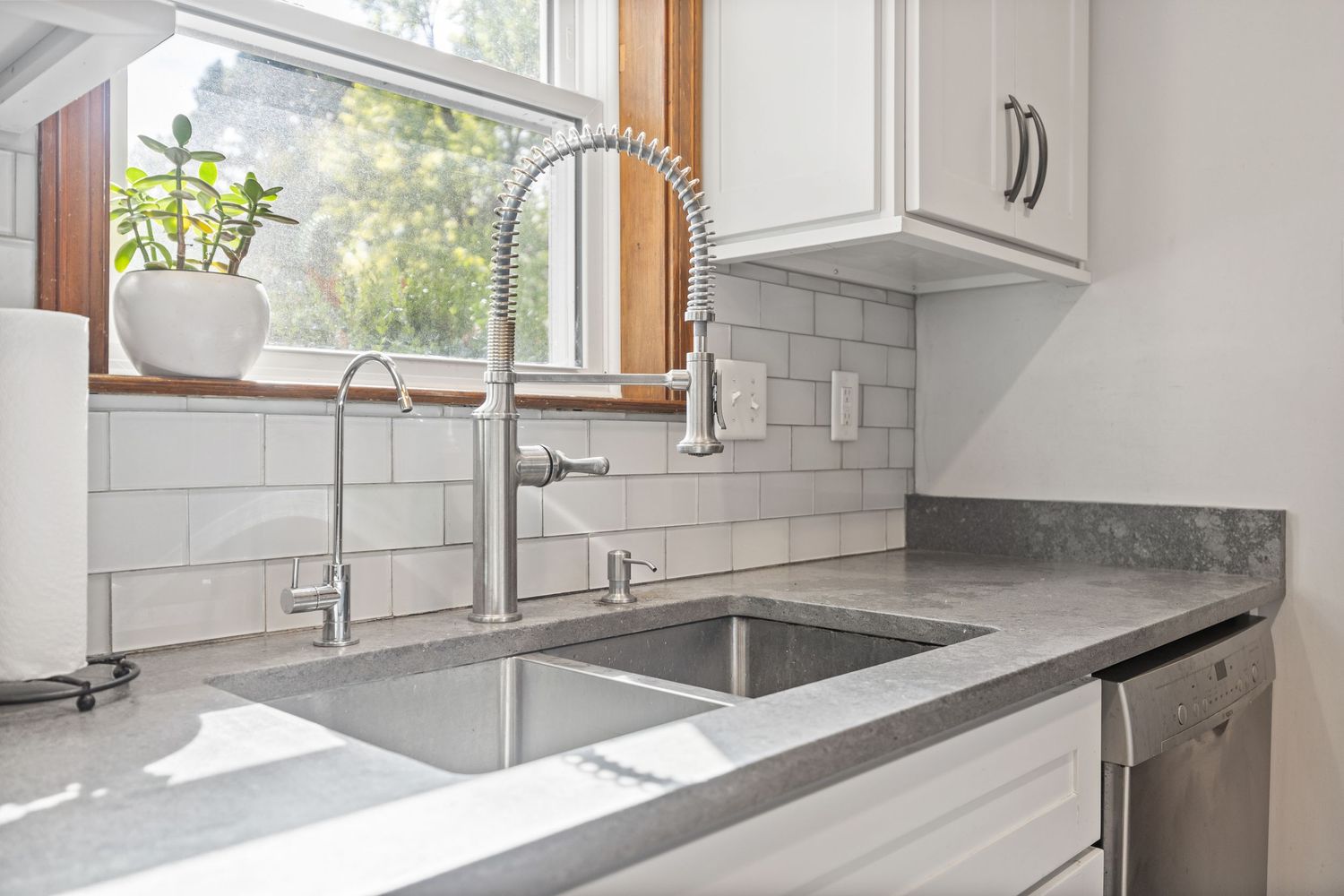 Bright modern kitchen with white cabinets, stainless appliances and grey countertops.