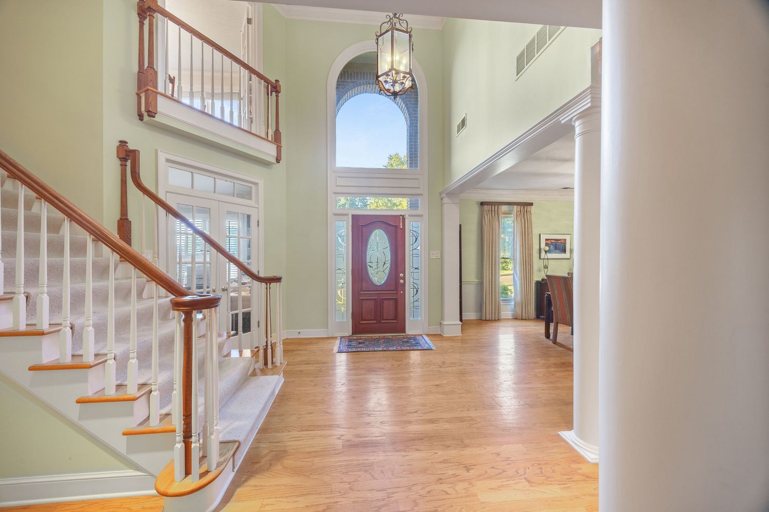 Elegant foyer with hardwood floors, red front door, and white staircase in a bright two-story entryway with sage walls.