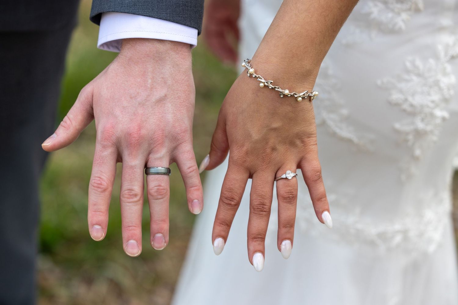 Close up detail shots of hands displaying wedding rings and jewelry against a white dress background.