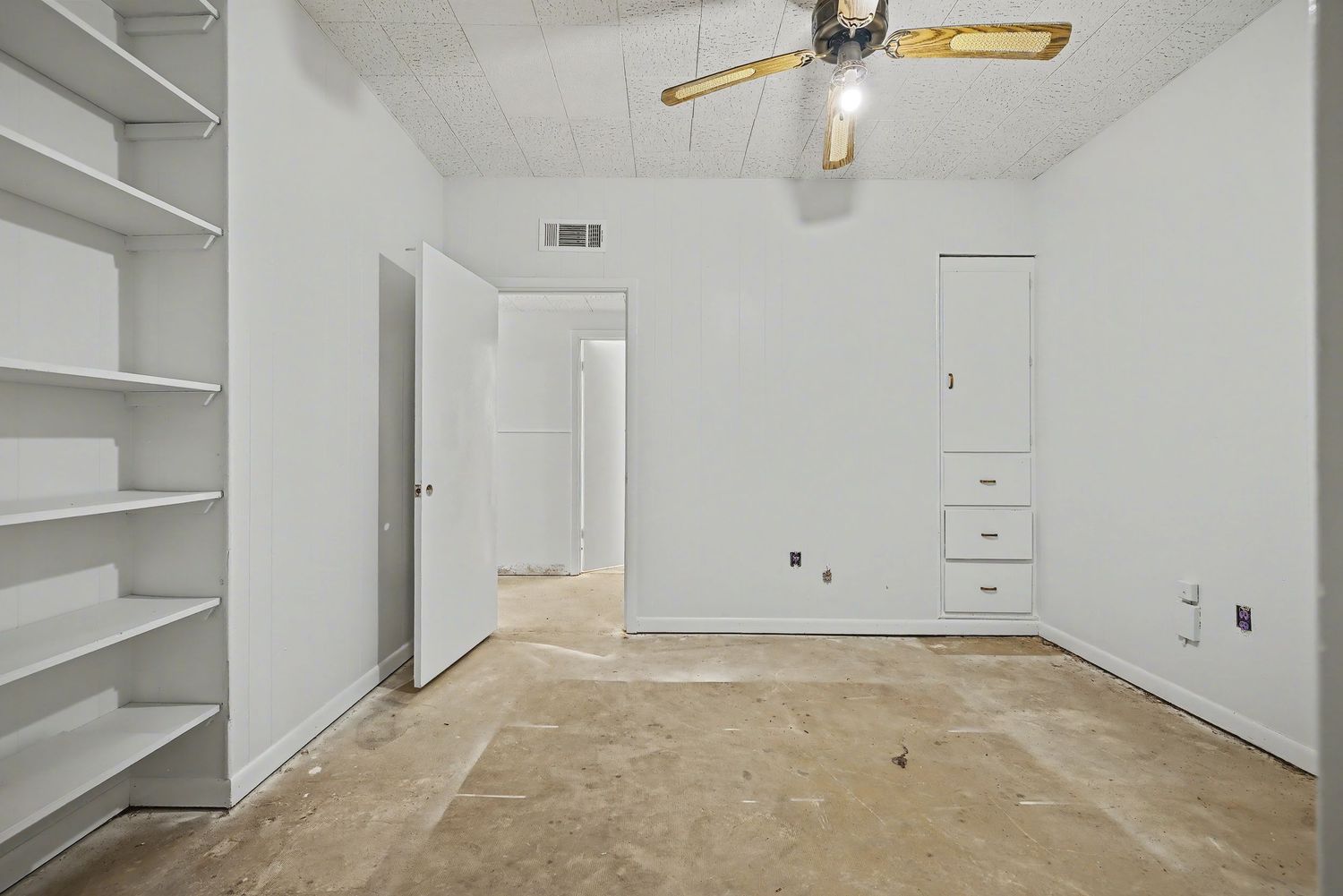 Interior view of empty room with white walls, ceiling fan, and built-in shelving along the walls.