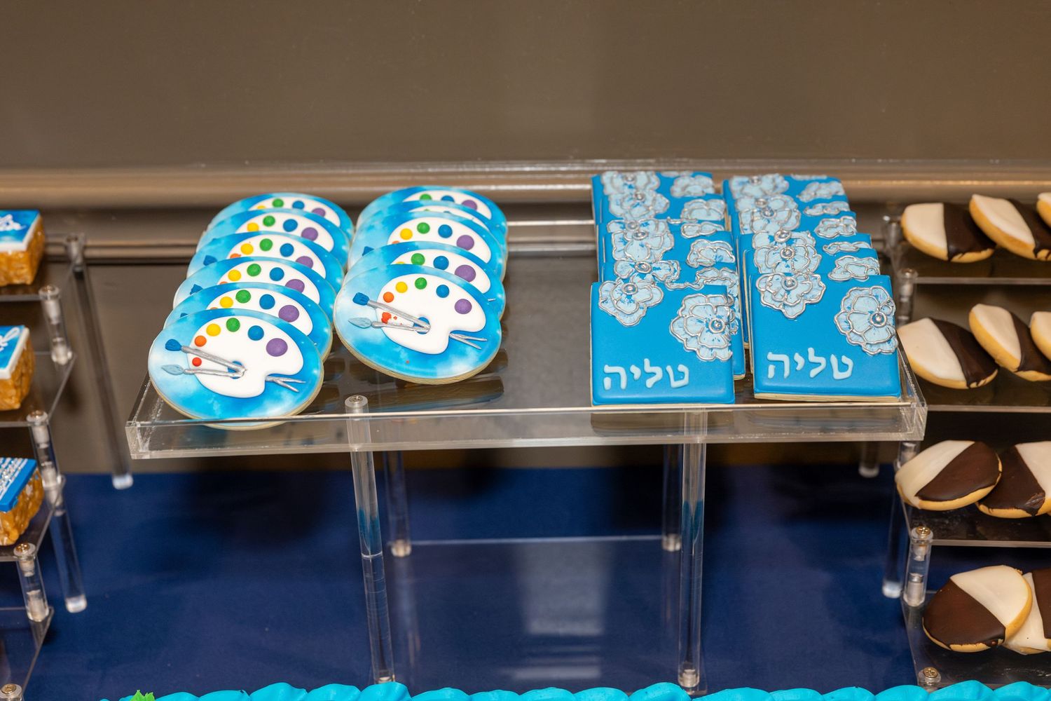 Blue decorated cookies with Hebrew text and panda designs displayed on a clear acrylic bakery shelf.