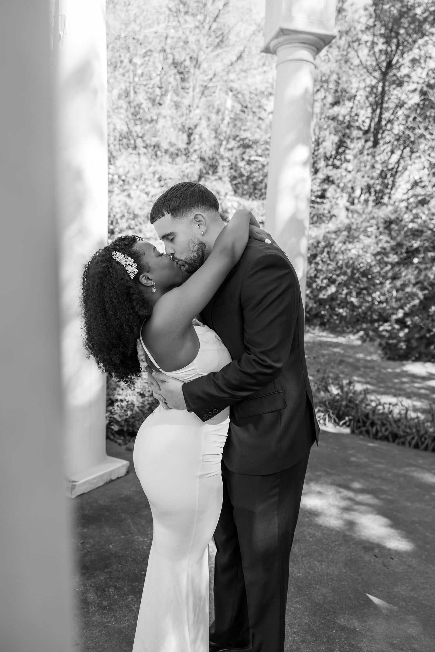 Black and white wedding portrait captured under elegant white columns outdoors.