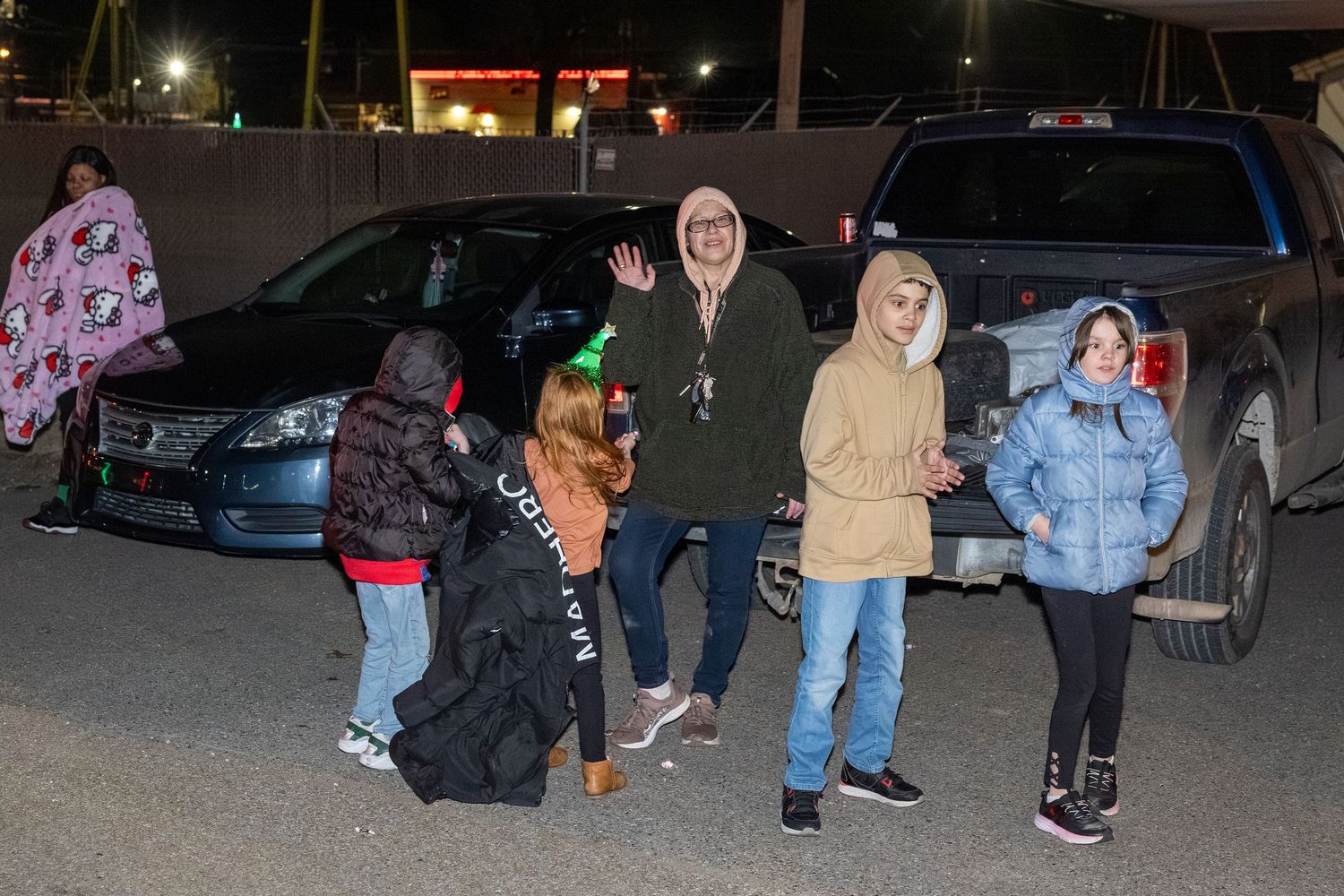 A group poses together in a parking lot at night with cars in the background.