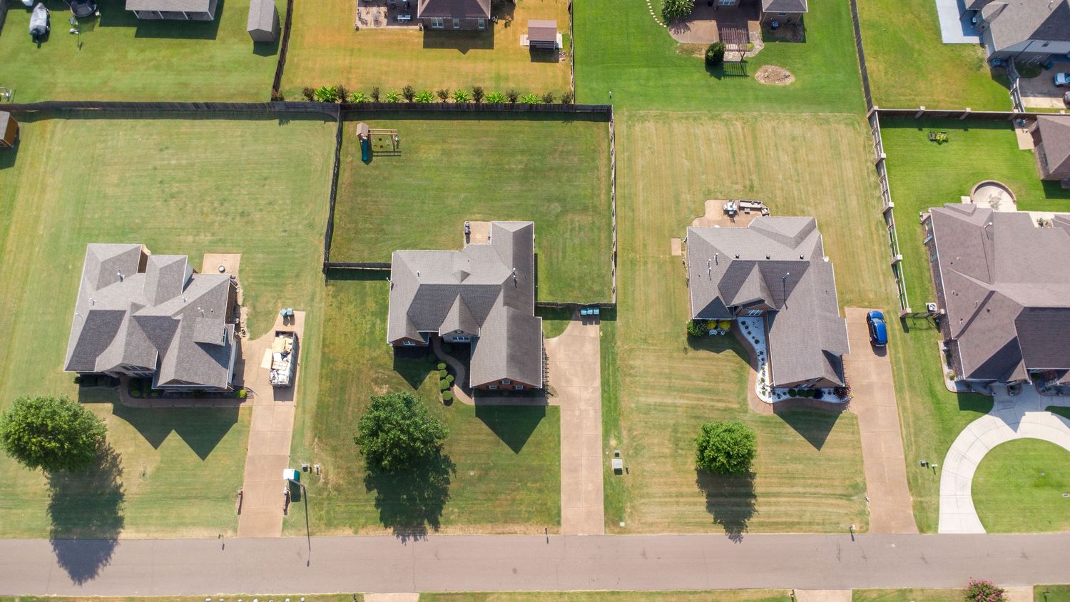 Aerial view of suburban neighborhood houses with green lawns and driveways arranged in neat rows.